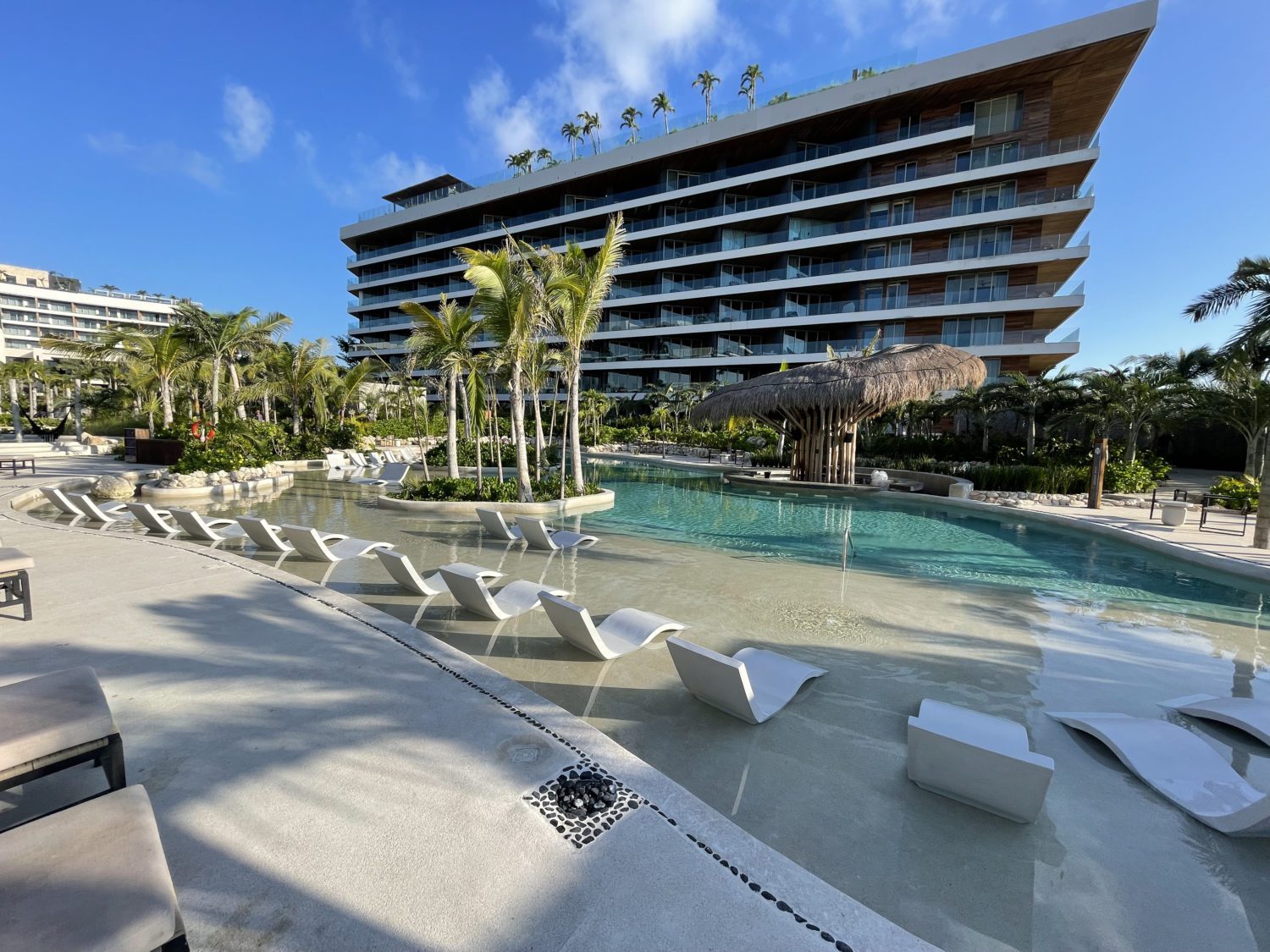 a hotel pool with lots of lounge chairs in the water and an island of palm trees in the middle 