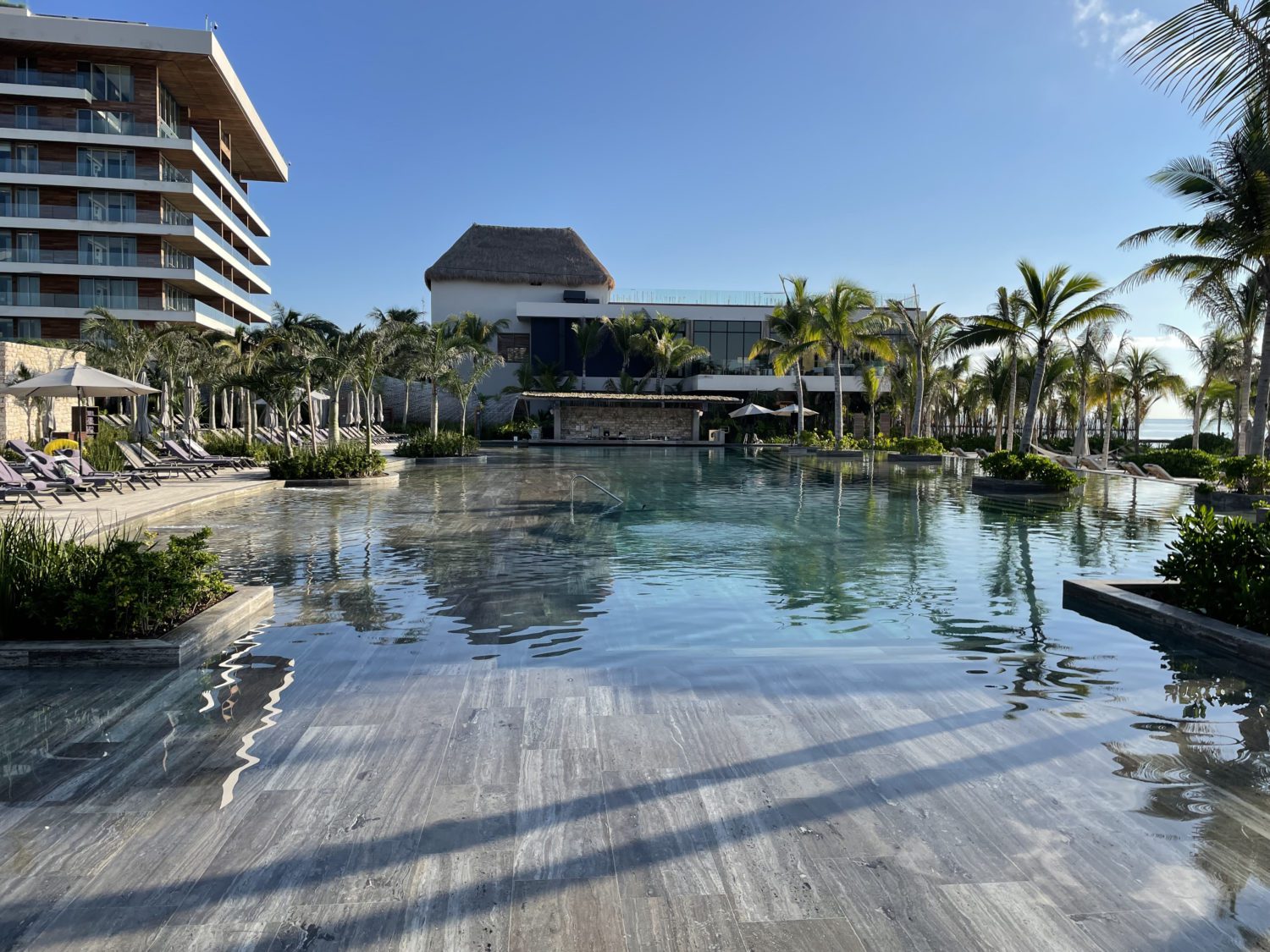 a swim up bar at the back of a long pool with palm trees all around