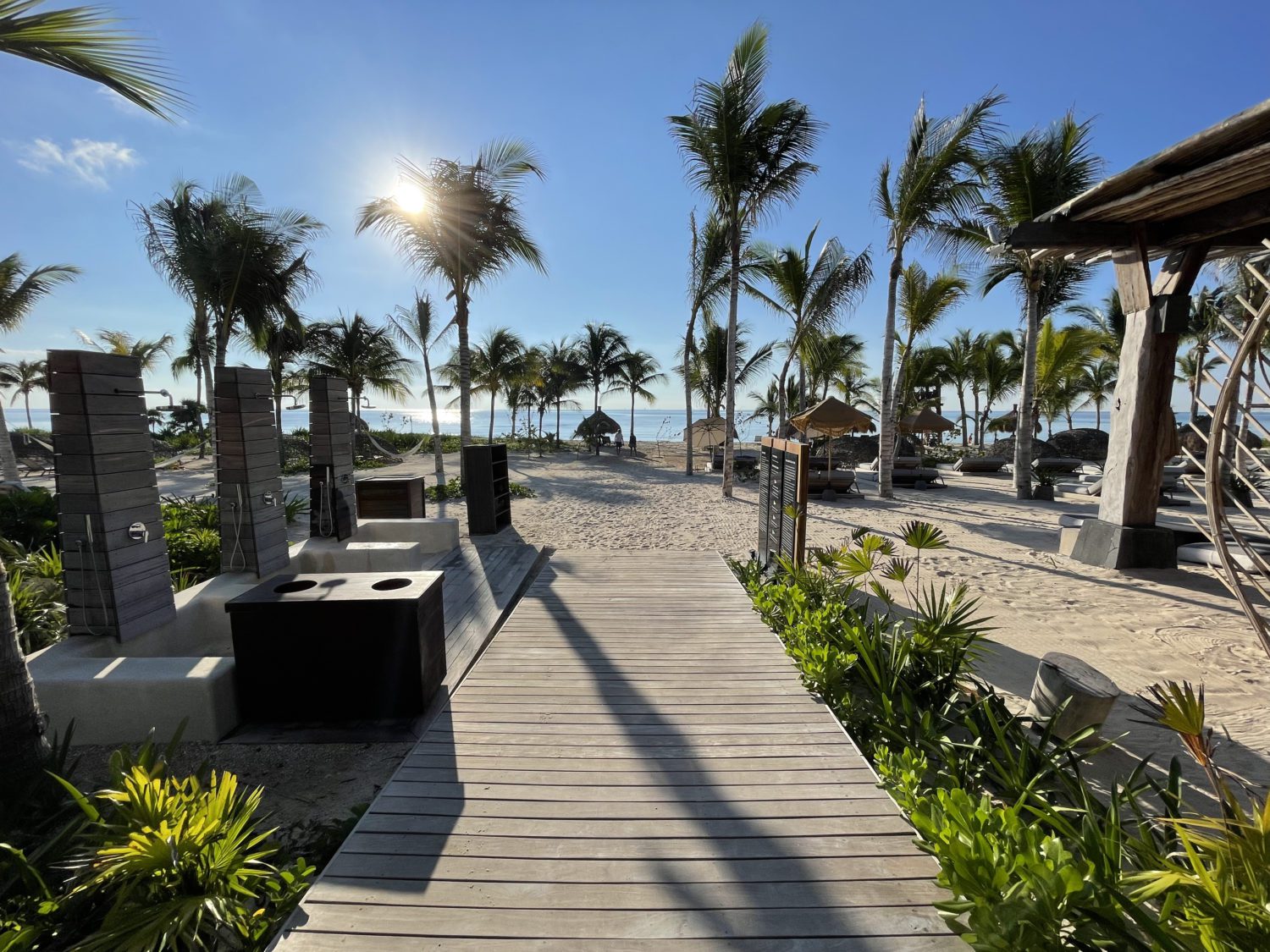 boardwalk leading to a beach with outdoor showers on the left and lots of palm trees. 