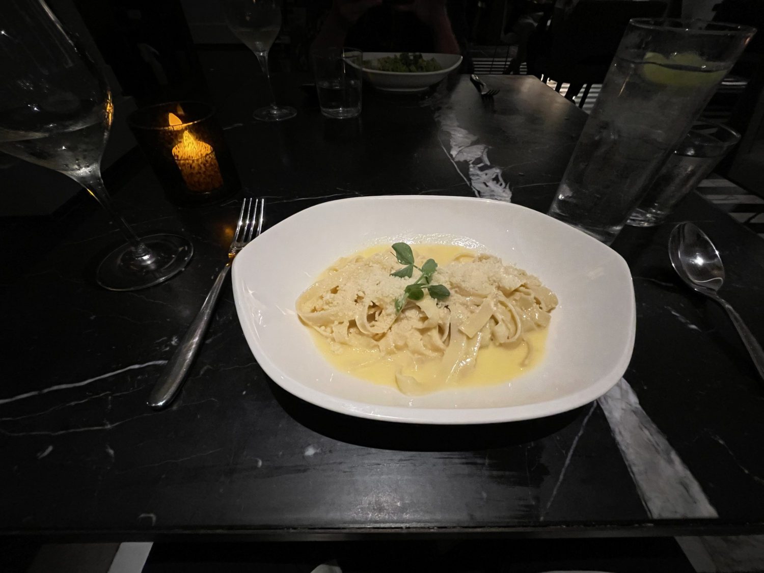 A white bowl of fettuccine Alfredo pasta with basil leaves on top