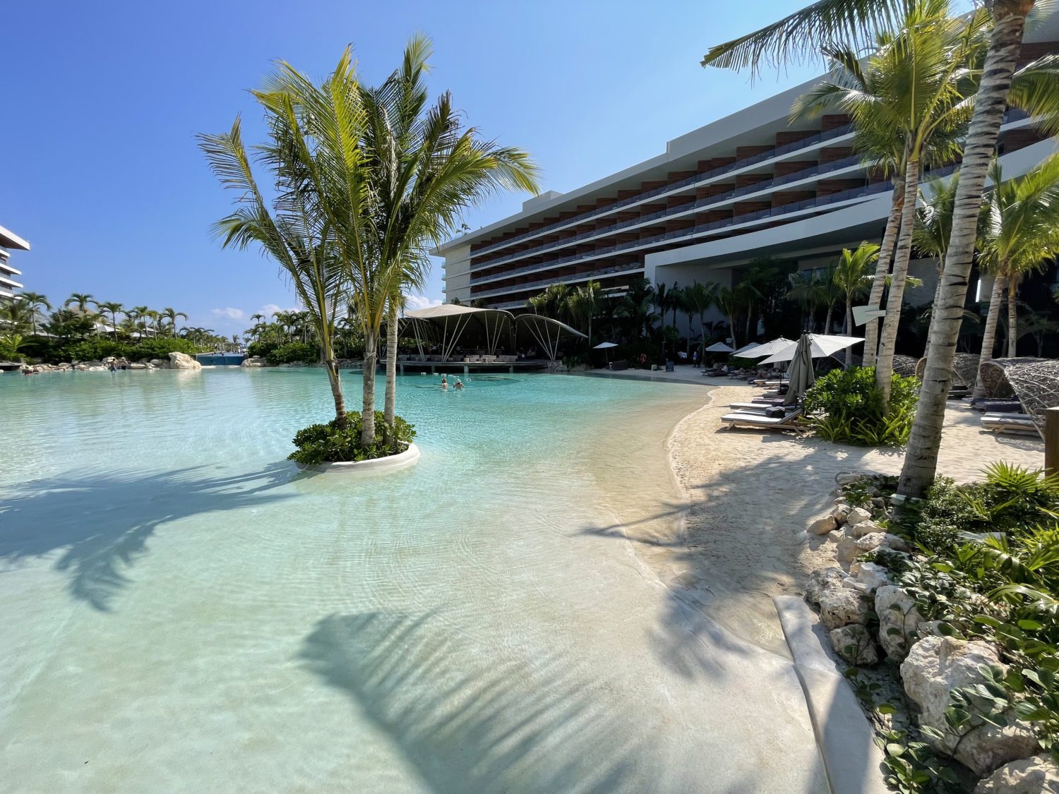 the lagoon pool with a sandy beach, and small islands with palm trees in the middle of the pool. 