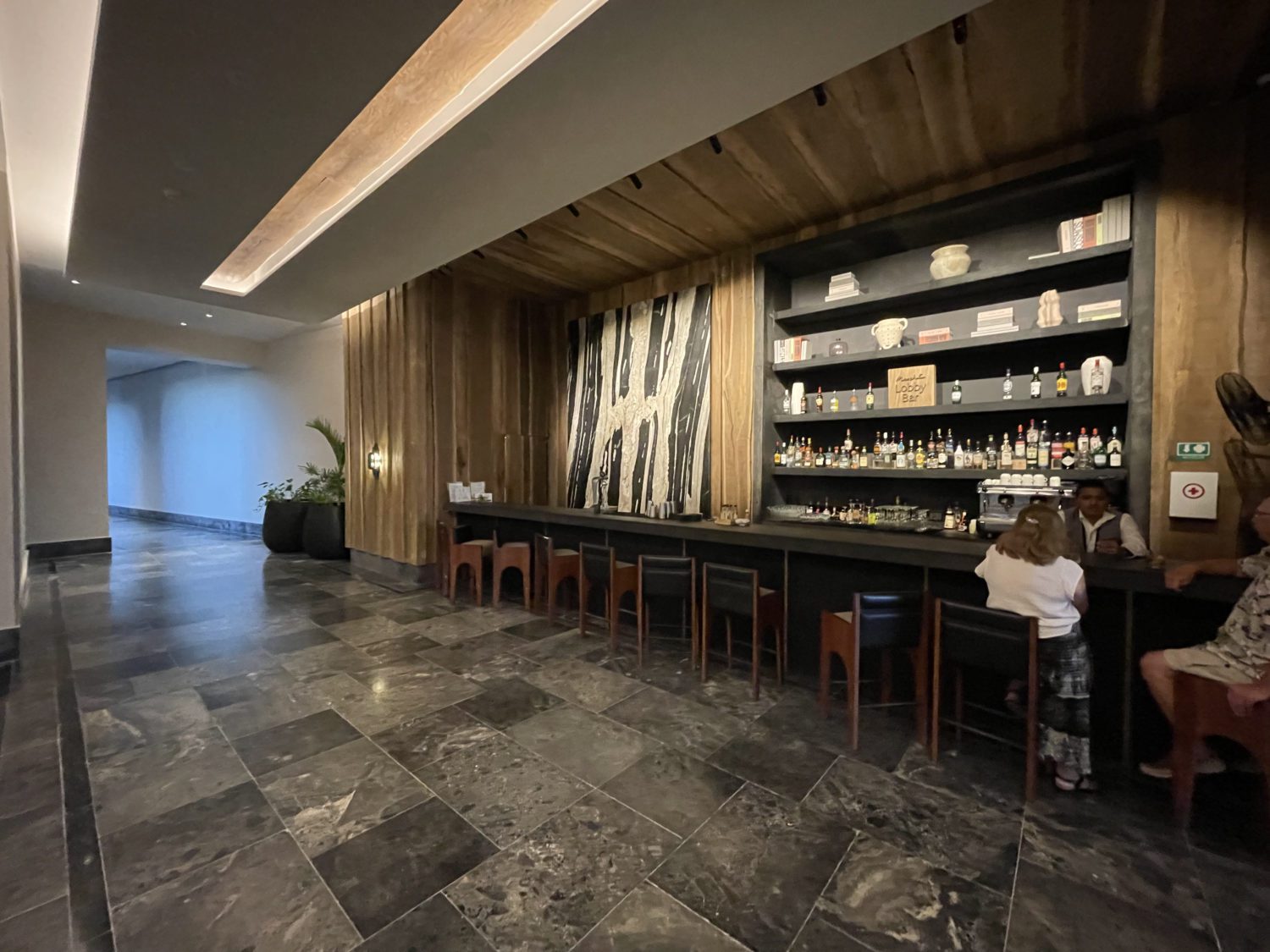 an unassuming bar in a hotel lobby with a few guests sitting on chairs talking to the bartender. 