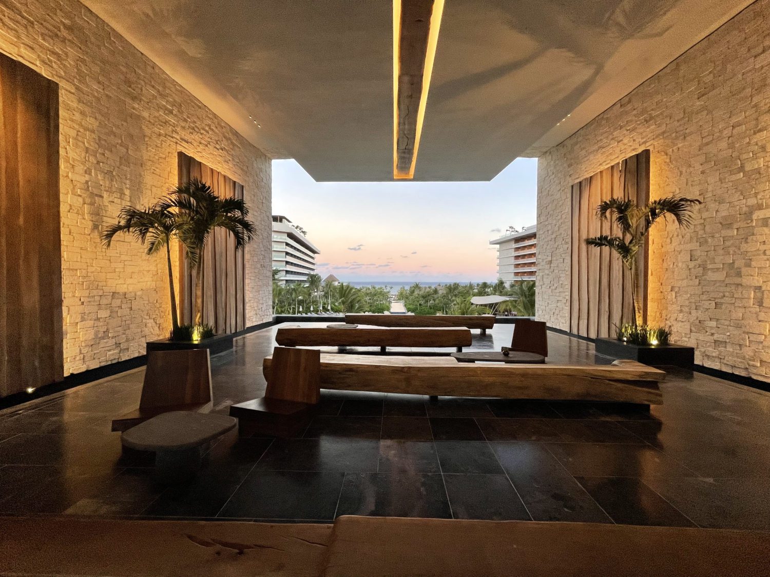 View of the ocean from the hotel lobby. The open-air space has moody lighting and three long benches made from tree trunks. 