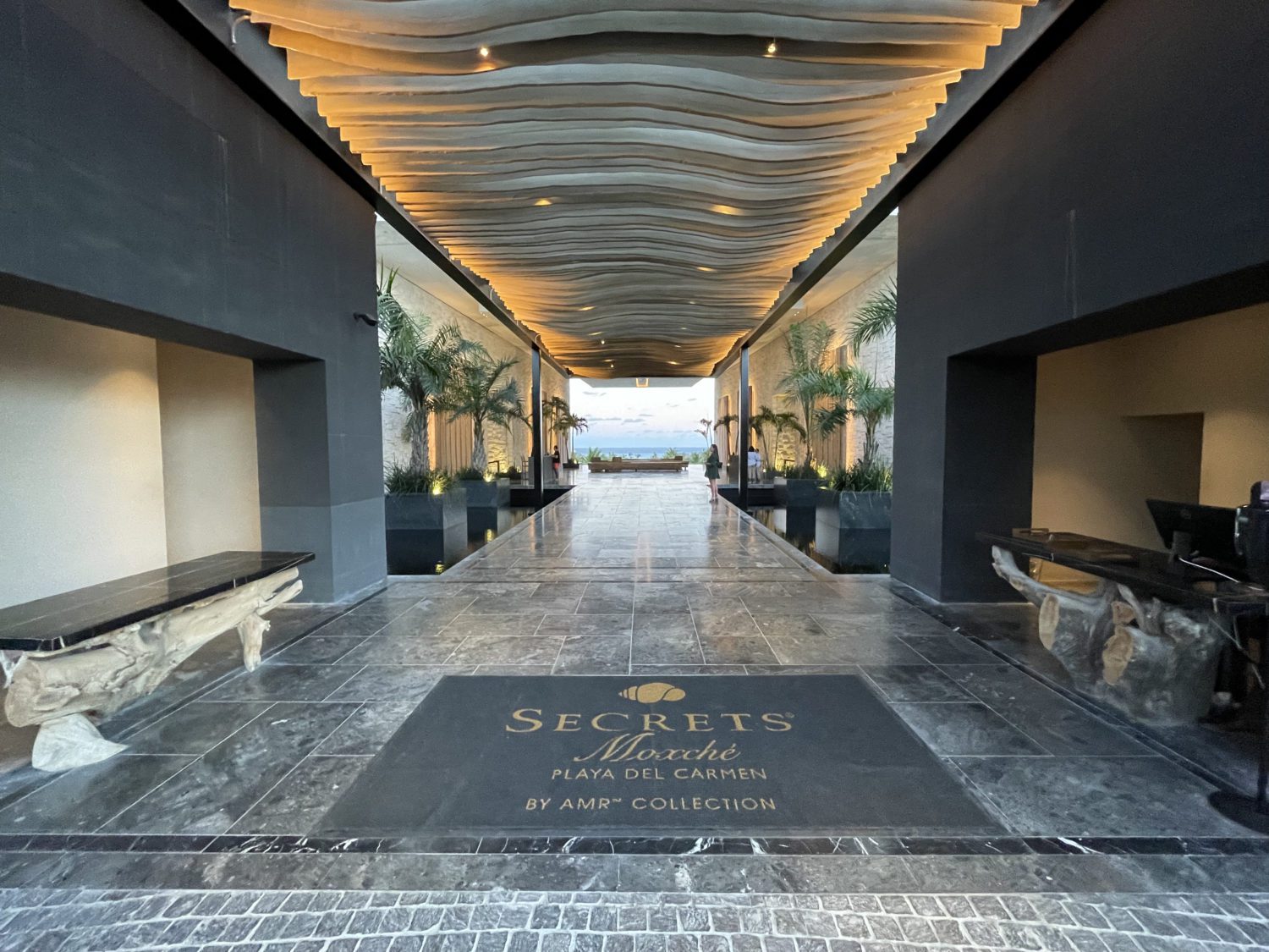 hotel entrance with dark stone floors and a floor mat that says Secrete Moxche Playa del Carmen