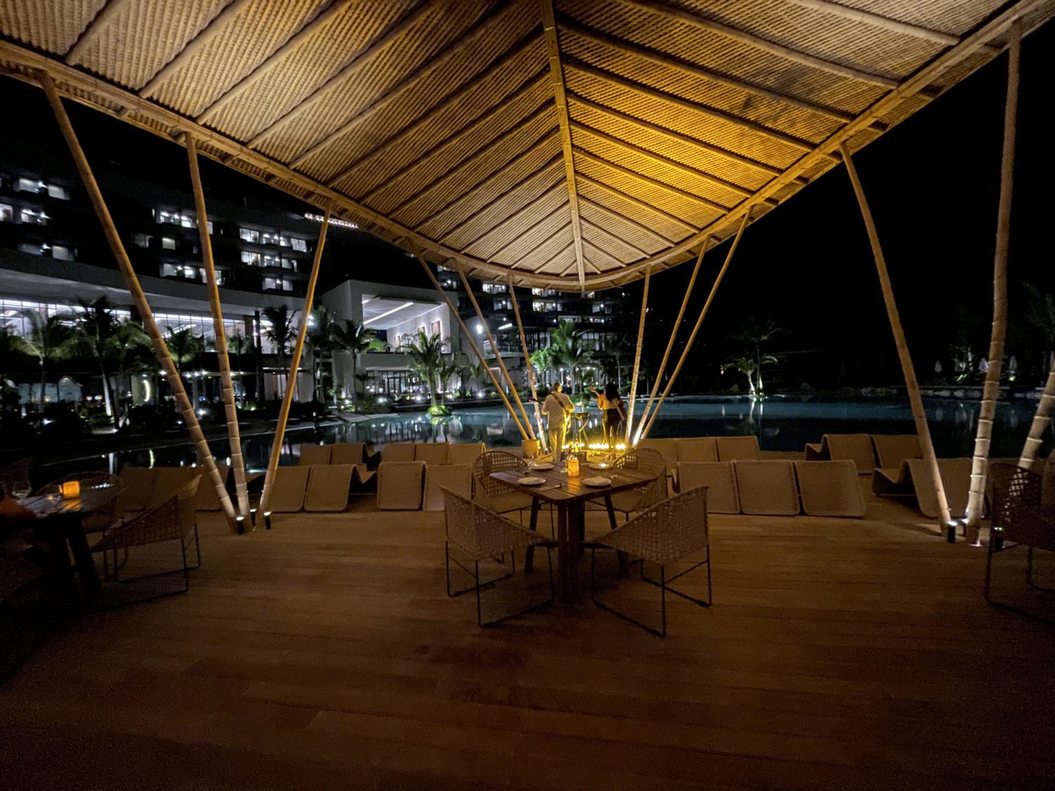 outdoor seating area at a hotel restaurant with mood lighting and a view of the pool. 