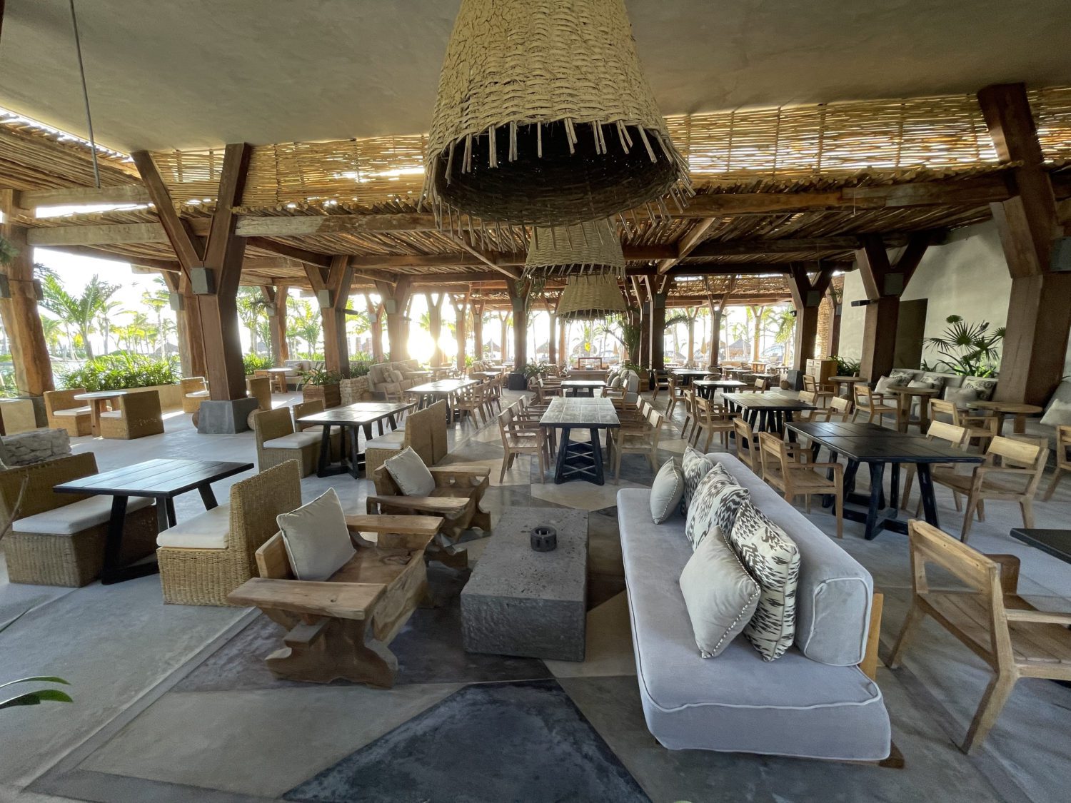 an open-air dining room with couches and armchairs and long dining tables