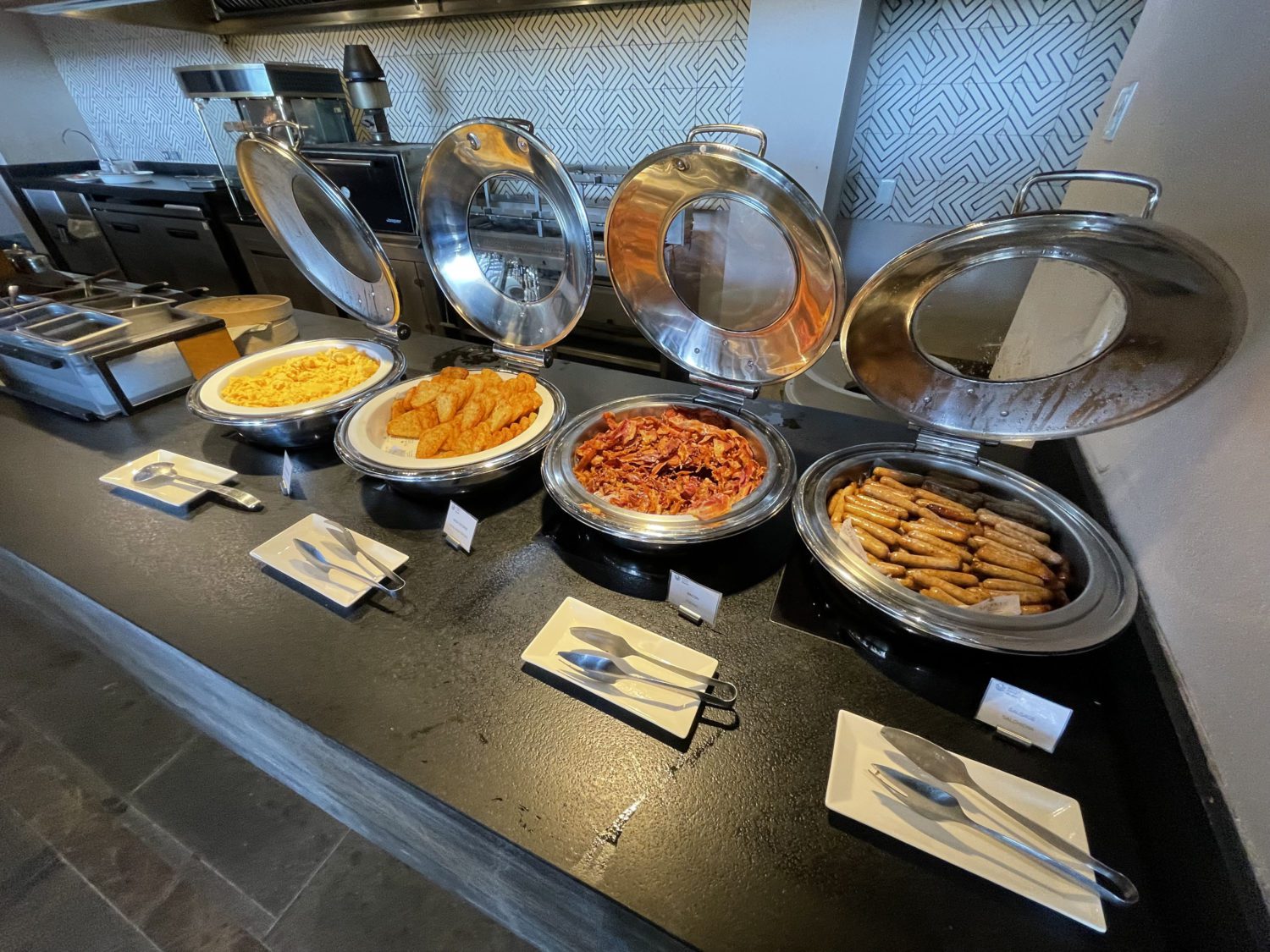 four chafing dishes with various breakfast meats at a hotel breakfast buffet