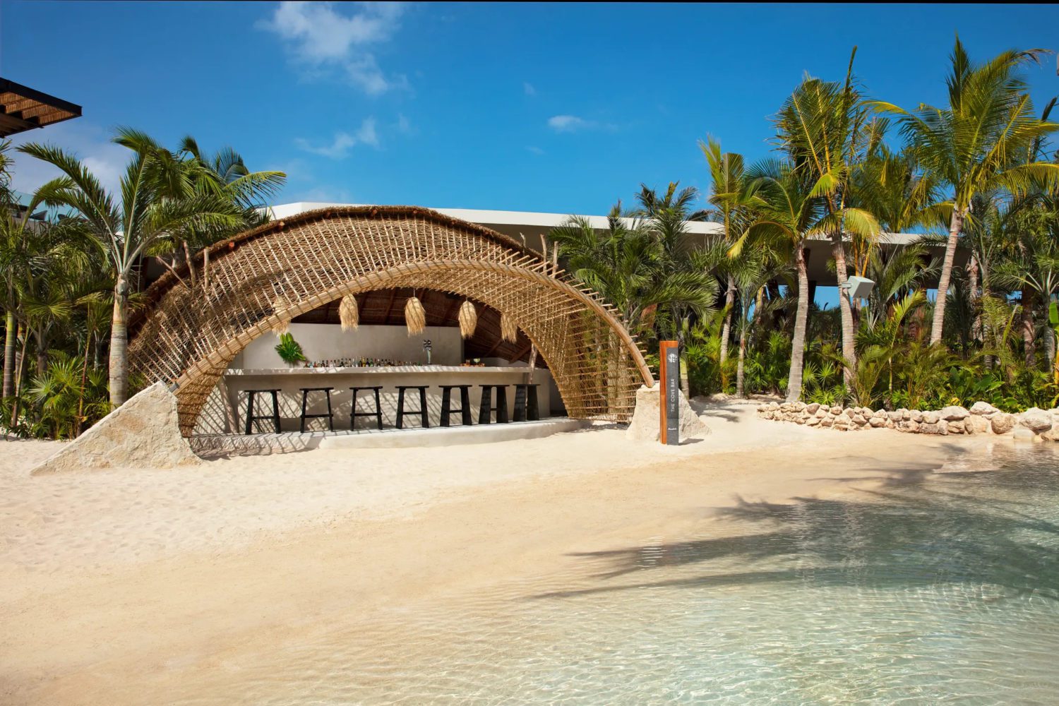 a small poolside bar on the sand with a straw canopy for shade. 