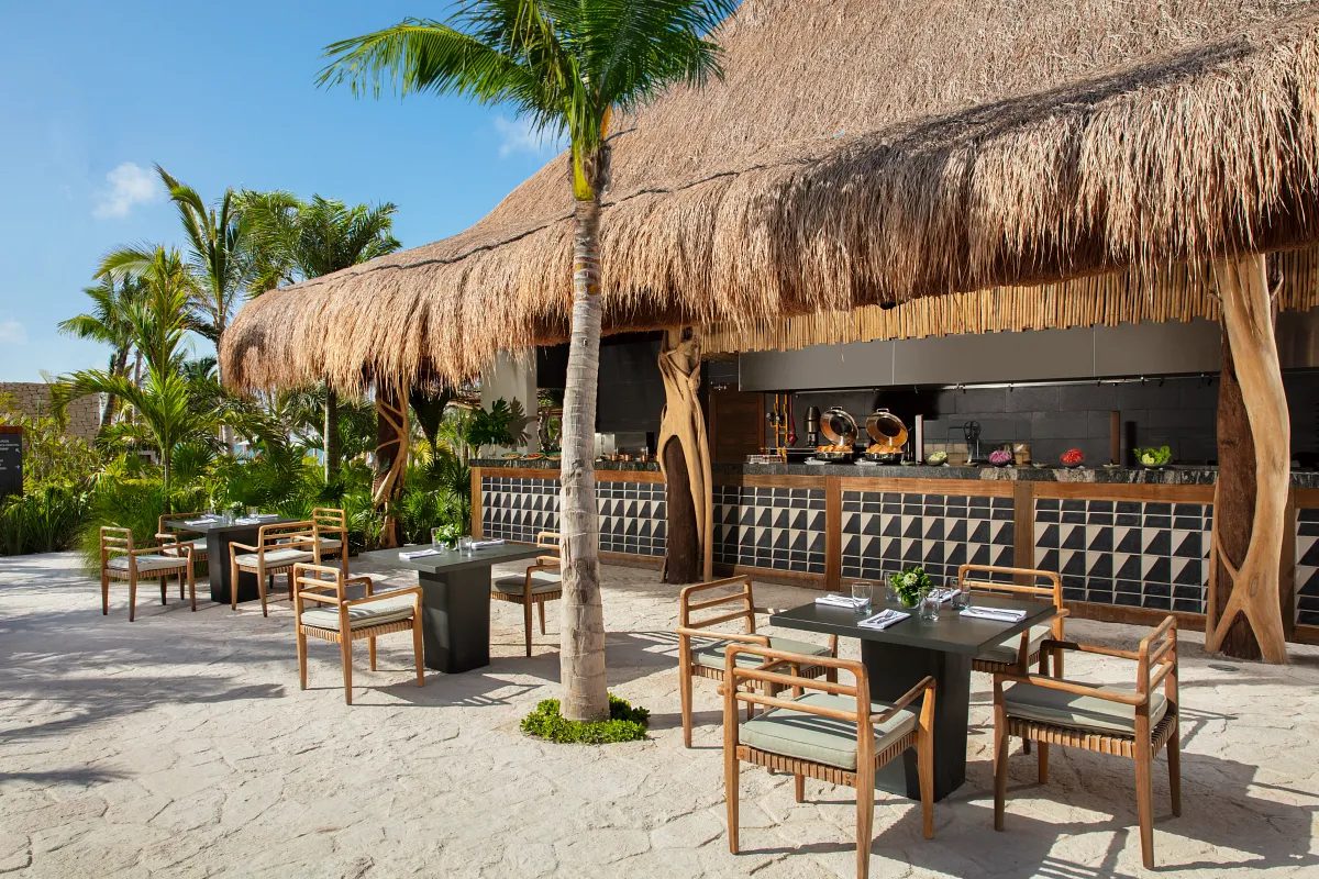 an outdoor restaurant with a thatched room, walk up bar and patio tables