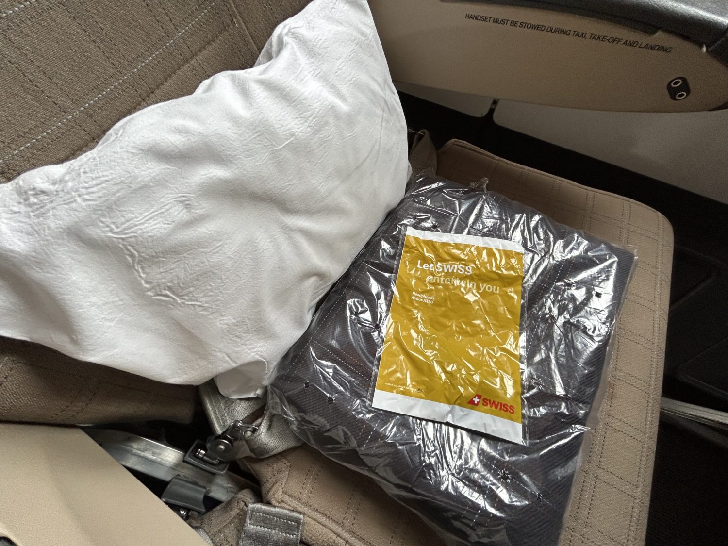 A pillow, blanket, and earbuds case on an airplane seat. 