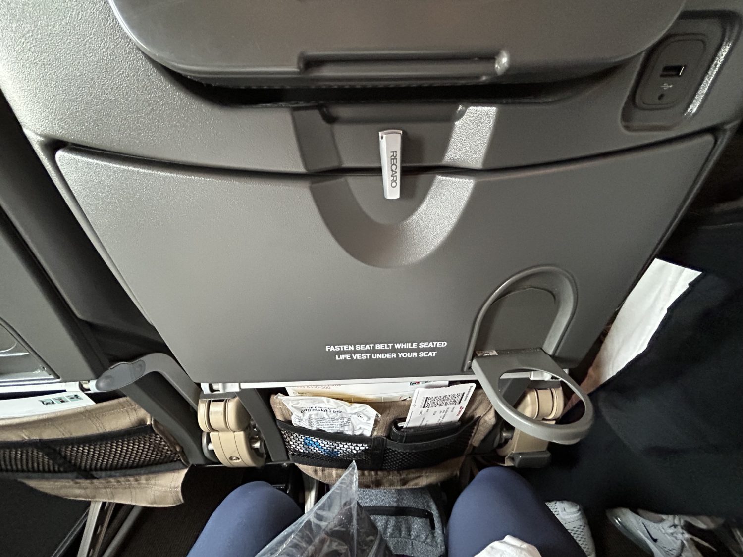 A tray table and its cupholder on an economy airplane seat. 