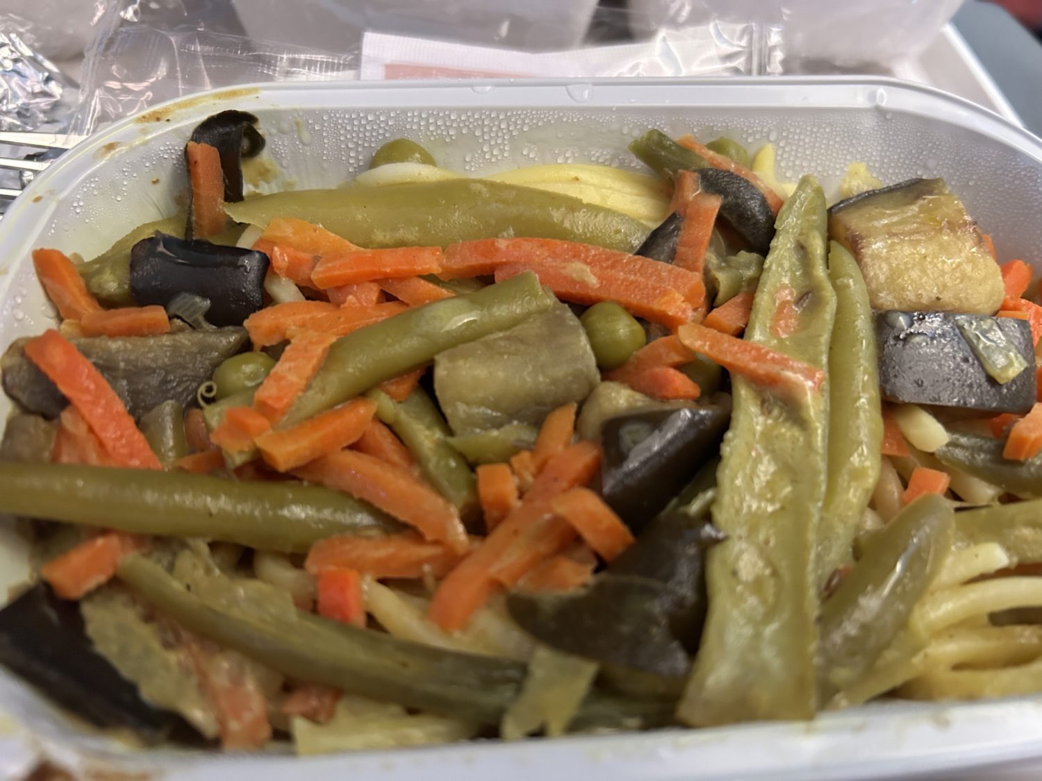 A close up of curry pasta in a plastic container on an airplane. 