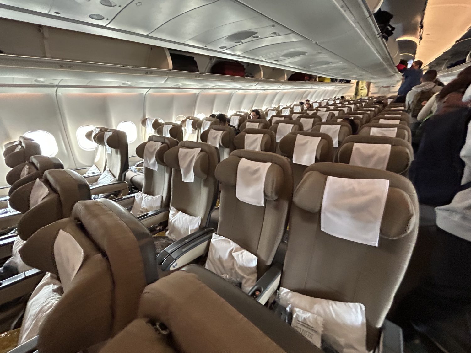 Rows and rows of brown SWISS economy airplane seats as passengers start to board an aircraft. 
