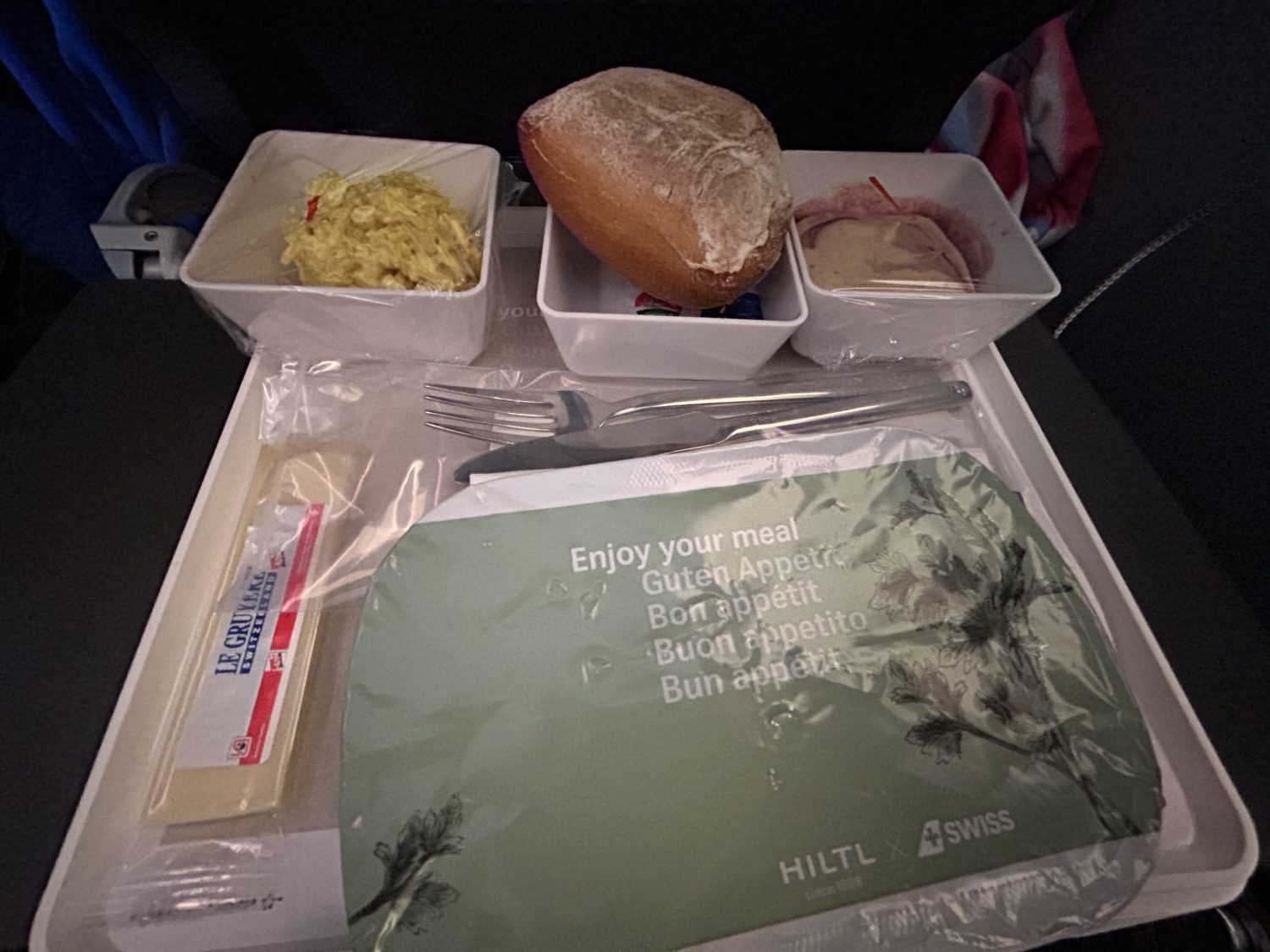 A tray of food given to economy passengers on SWISS Airlines including bread, a dessert, a side, and some cheese. 