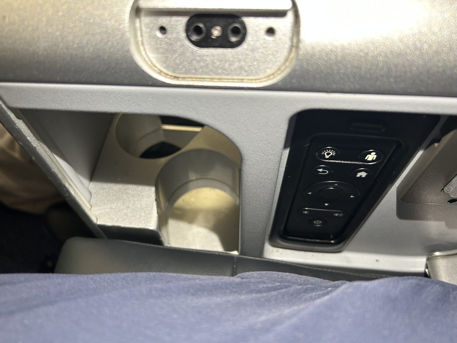 A water bottle holder and remote control on the side of an airplane seat. 