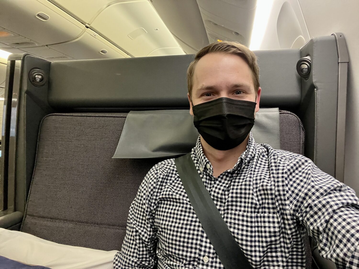 man in a mask smiling inside of a business class suite