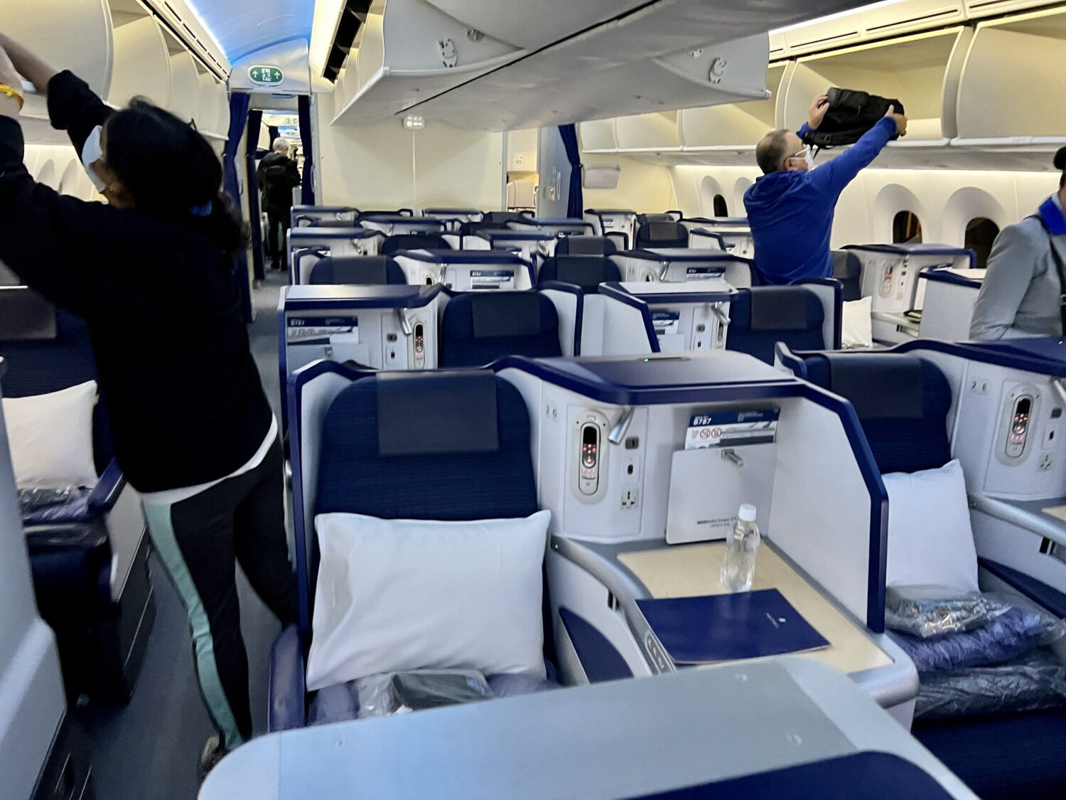 a cabin of business class seats with passengers putting bags in the overhead bins