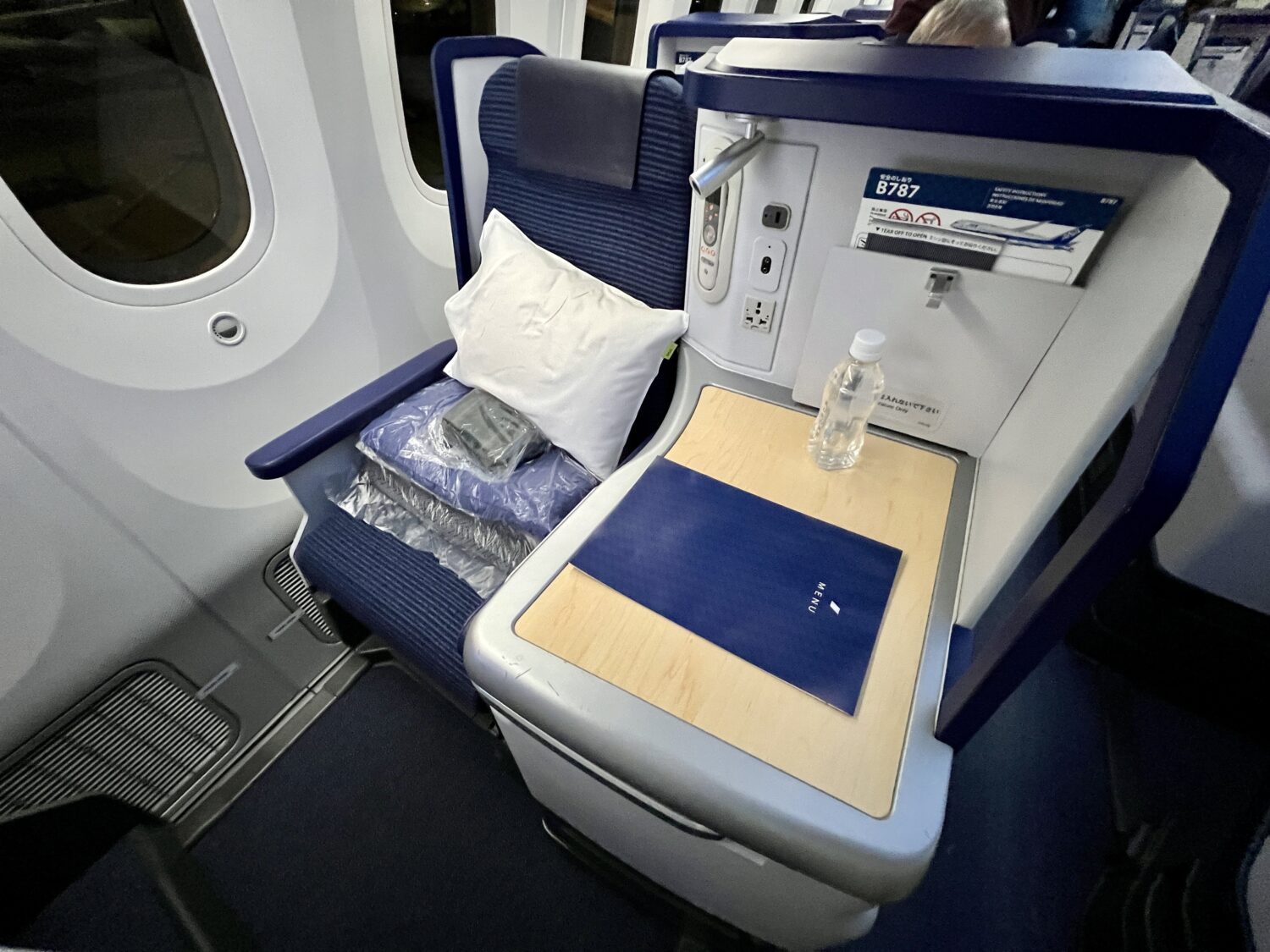 a blue business class seat with amenities on the seat and a water bottle on the table