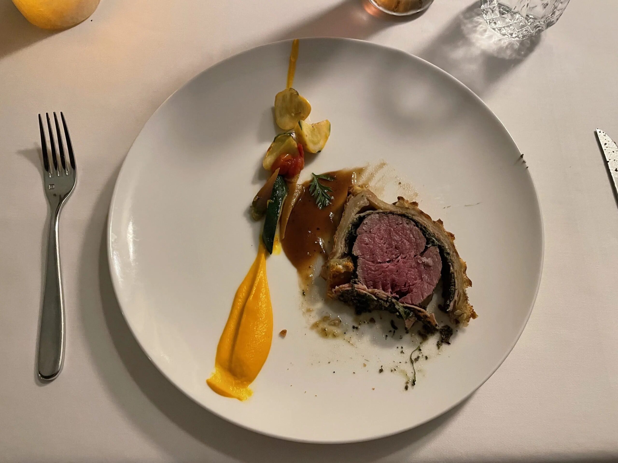 A dish with a small cut of meat, and a few drizzles of sauces on the side. 