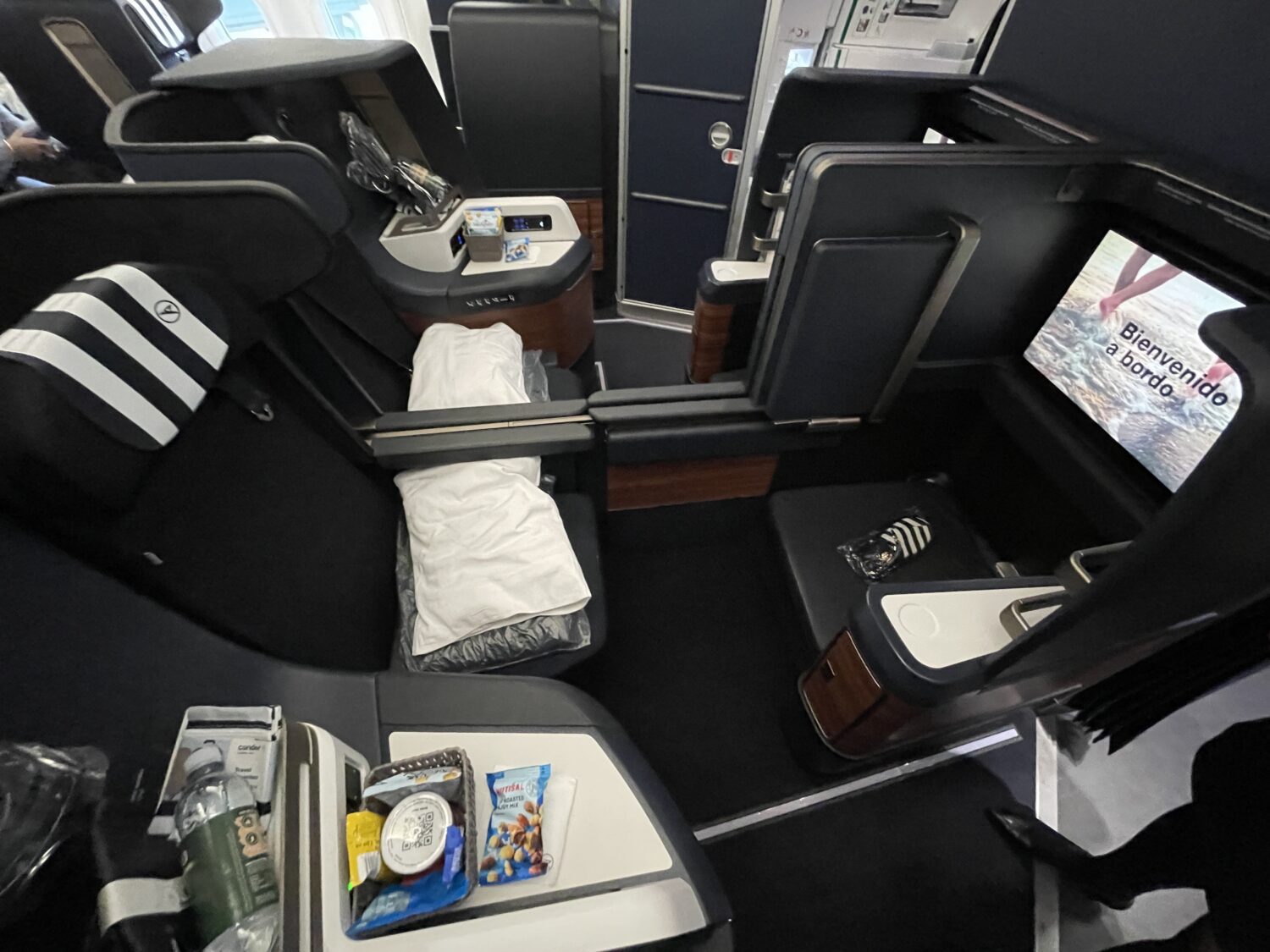 a business class seat with snacks, a water bottle, and a pillow 