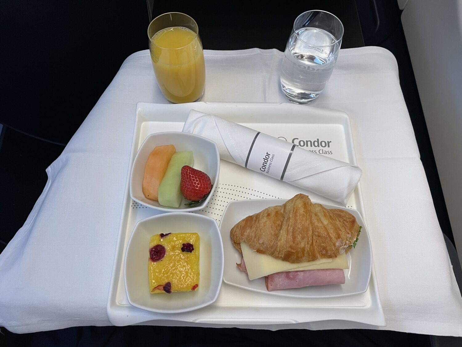 orange juice, water, fruit, and a croissant 