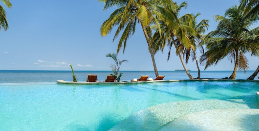 a crystal blue infinity pool surrounded by chairs and palm trees overlooking the ocean