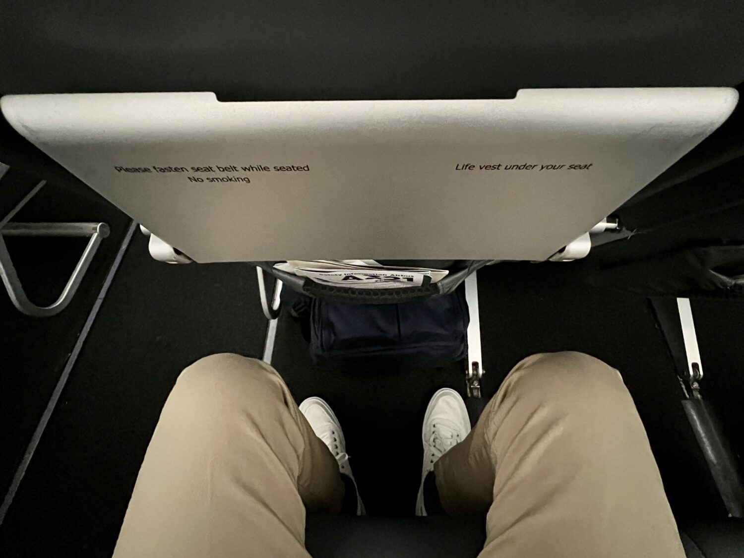 legs behind a plane seat with a backpack sticking out