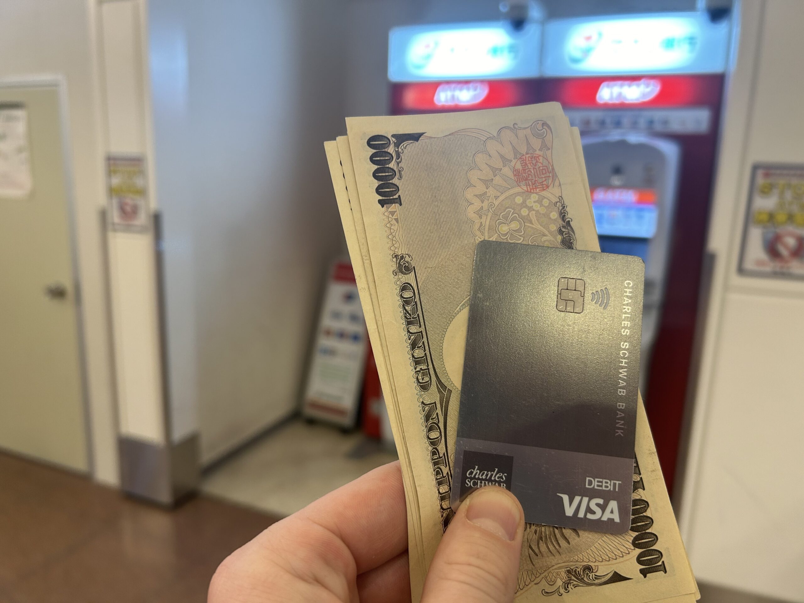 Charles Schwab Debit card and yen in being held in front of an ATM machine in Japan