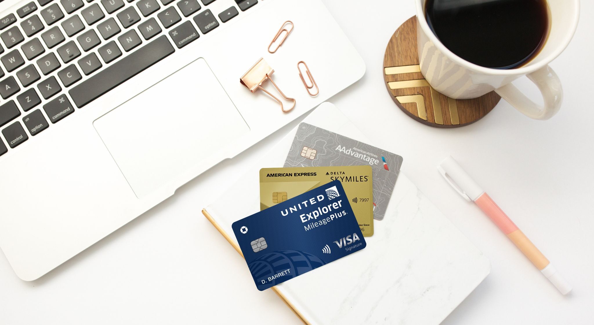 United, Delta, and American Airlines credit cards with a laptop and a cup of coffee on top of a desk.