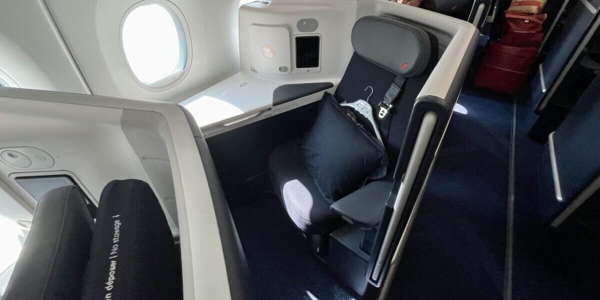 a business class seat with navy blue cushions and a pillow and blanket