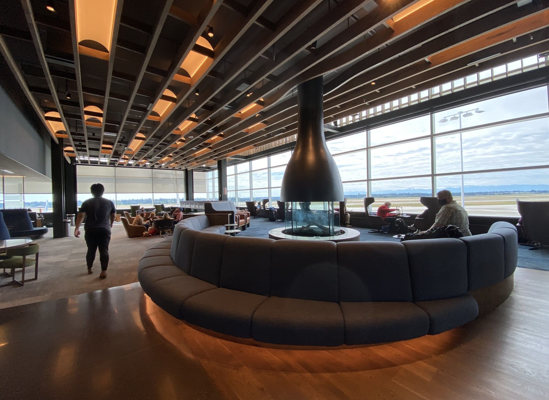 a large circular sofa built around a fireplace in a long room with many windows