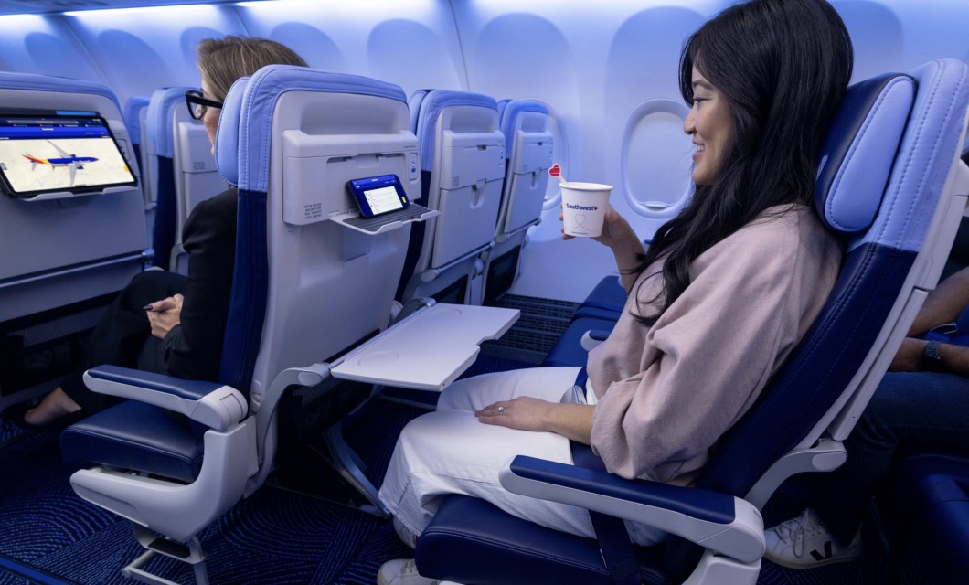a woman sitting in an airplane seat watching her phone with a coffee cup in hand