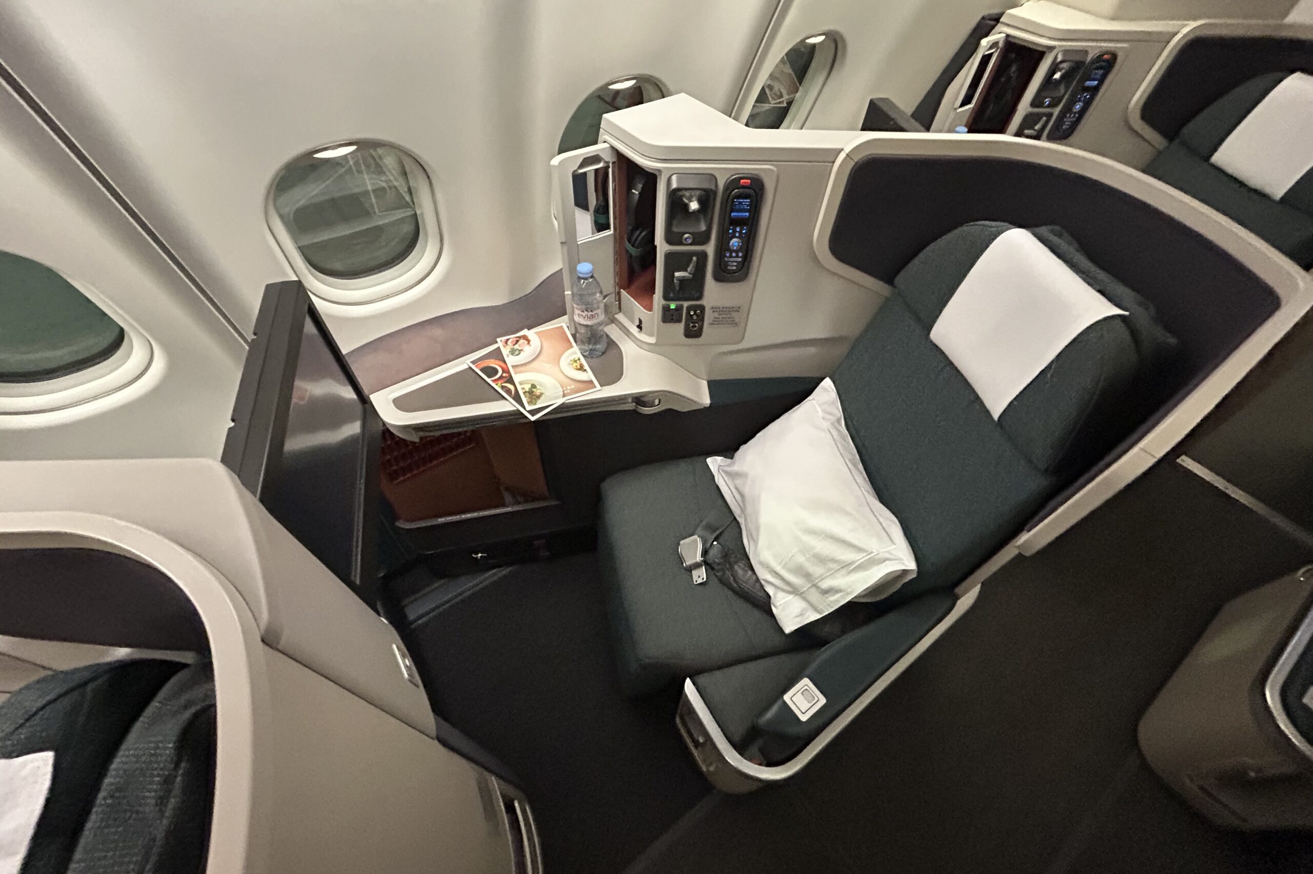 a green and white business class seat with a pillow, water bottle, and menus. 