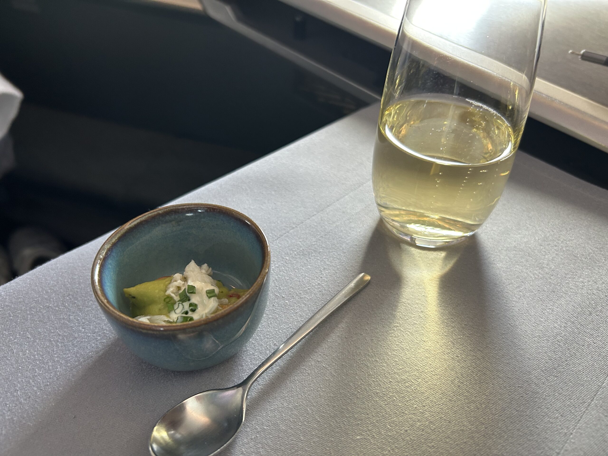 A dish of avocado mousse and a glass of champagne sitting on an airplane tray table.