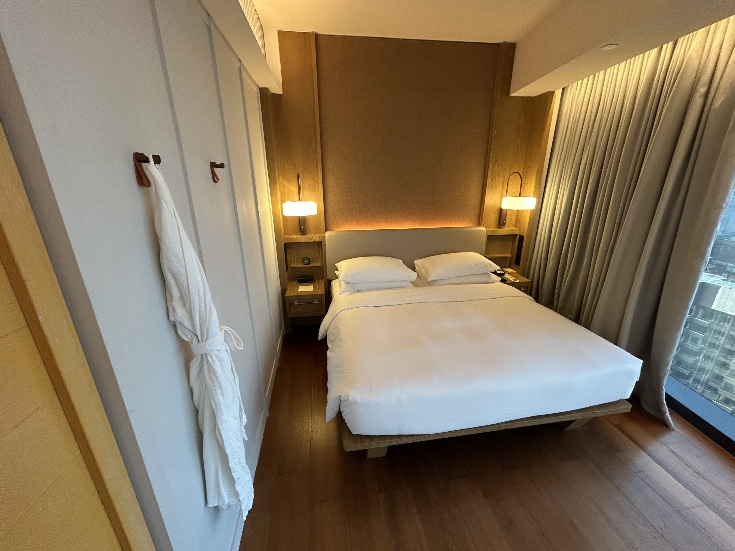 a king size bed with two bedside lamps. a bathrobe is hanging on the hook nearby. 