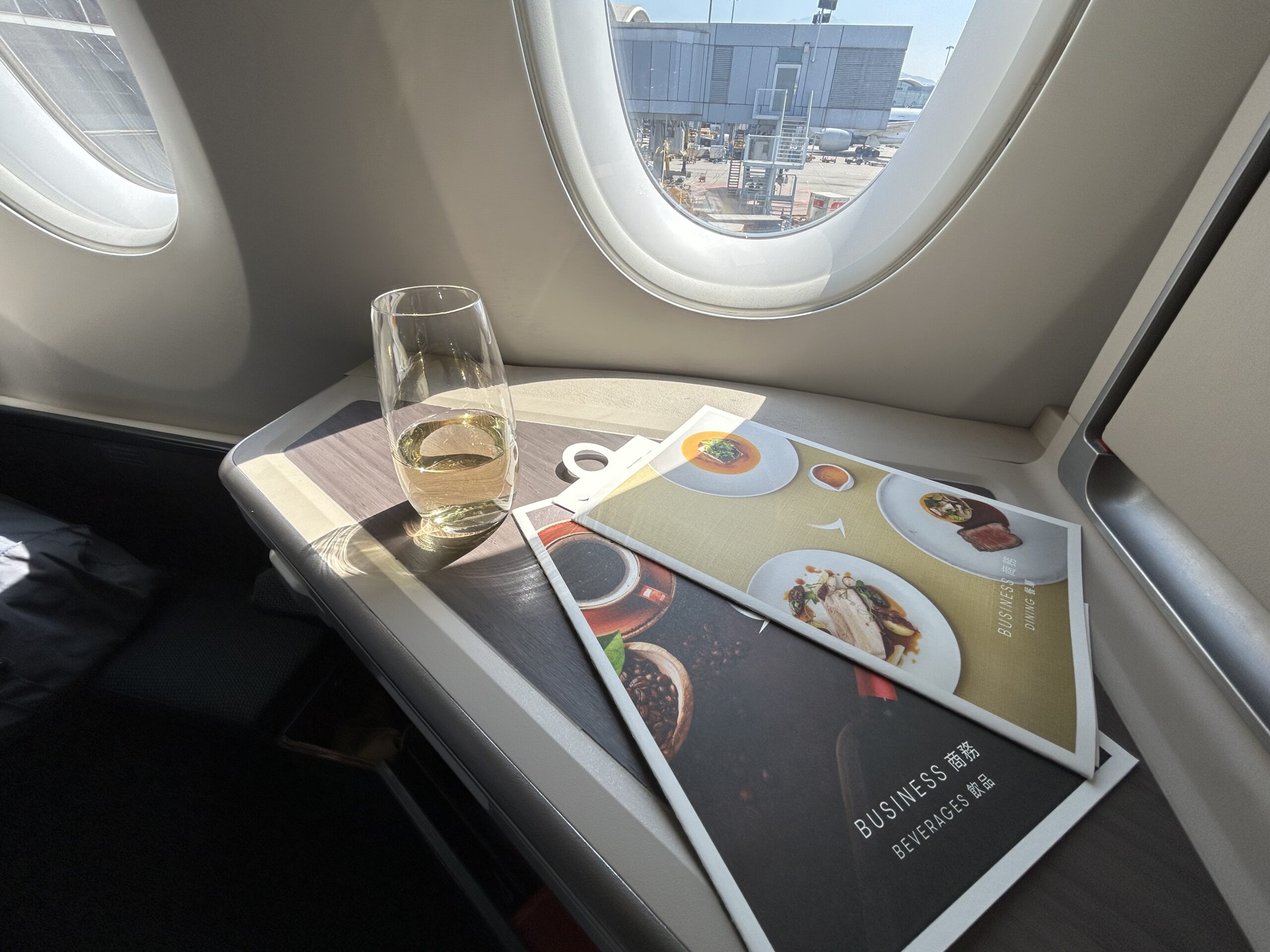 a glass of champagne sitting in the sun on the side table of an airplane business class seat