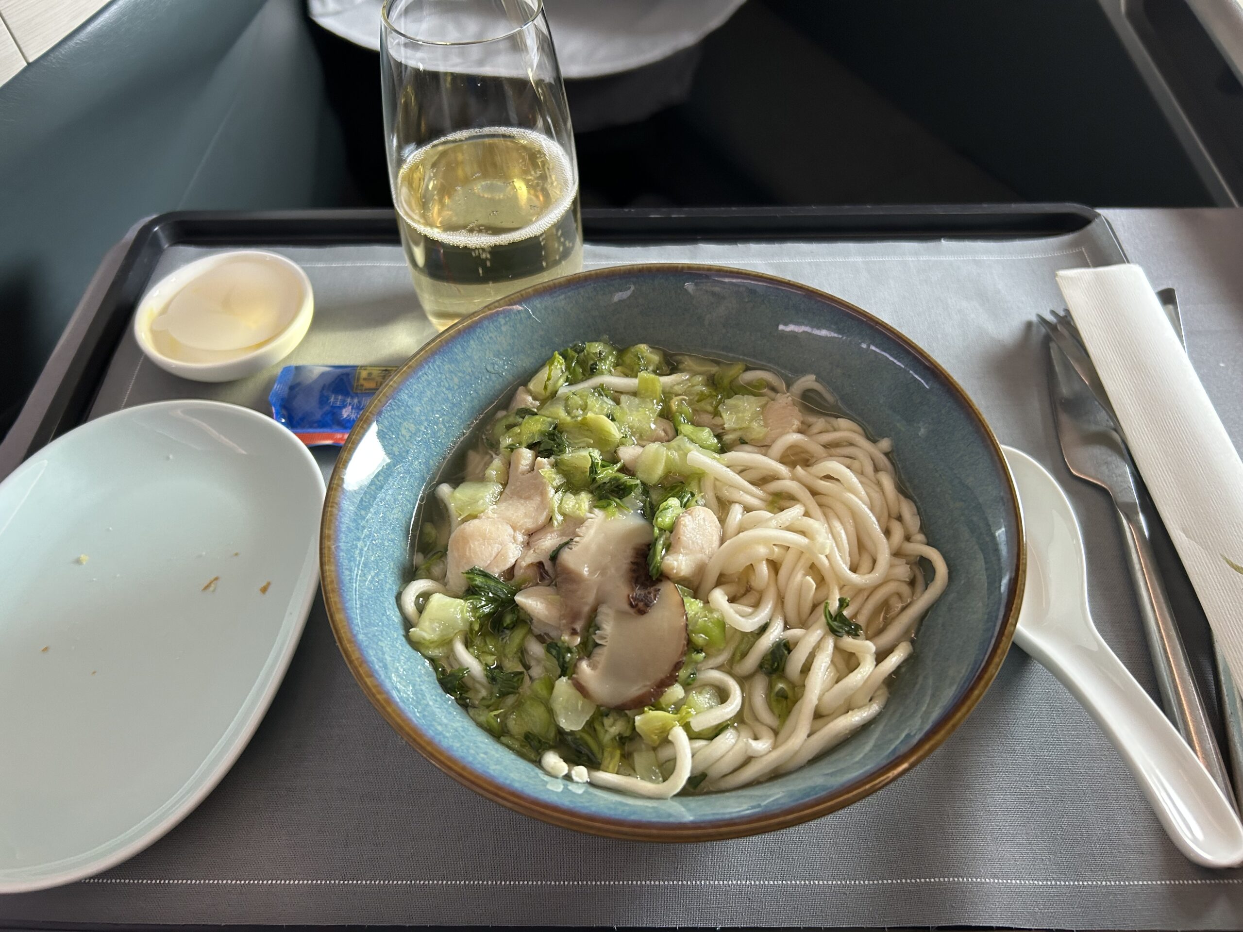 A bowl of chicken noodle soup and a glass of champagne on an airline tray table. 