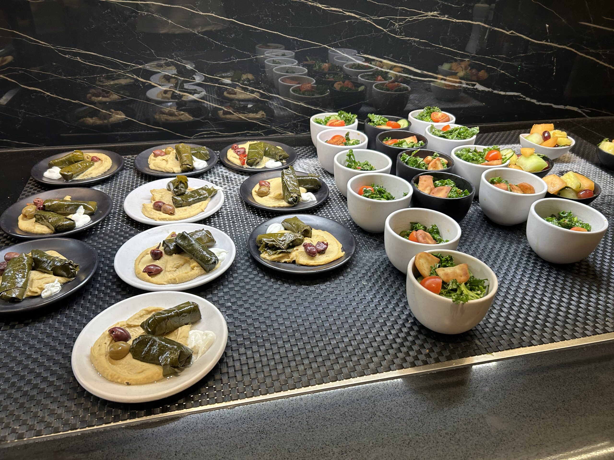 small plates with hummus and grape leaves and bowls with kale salad on a buffet 