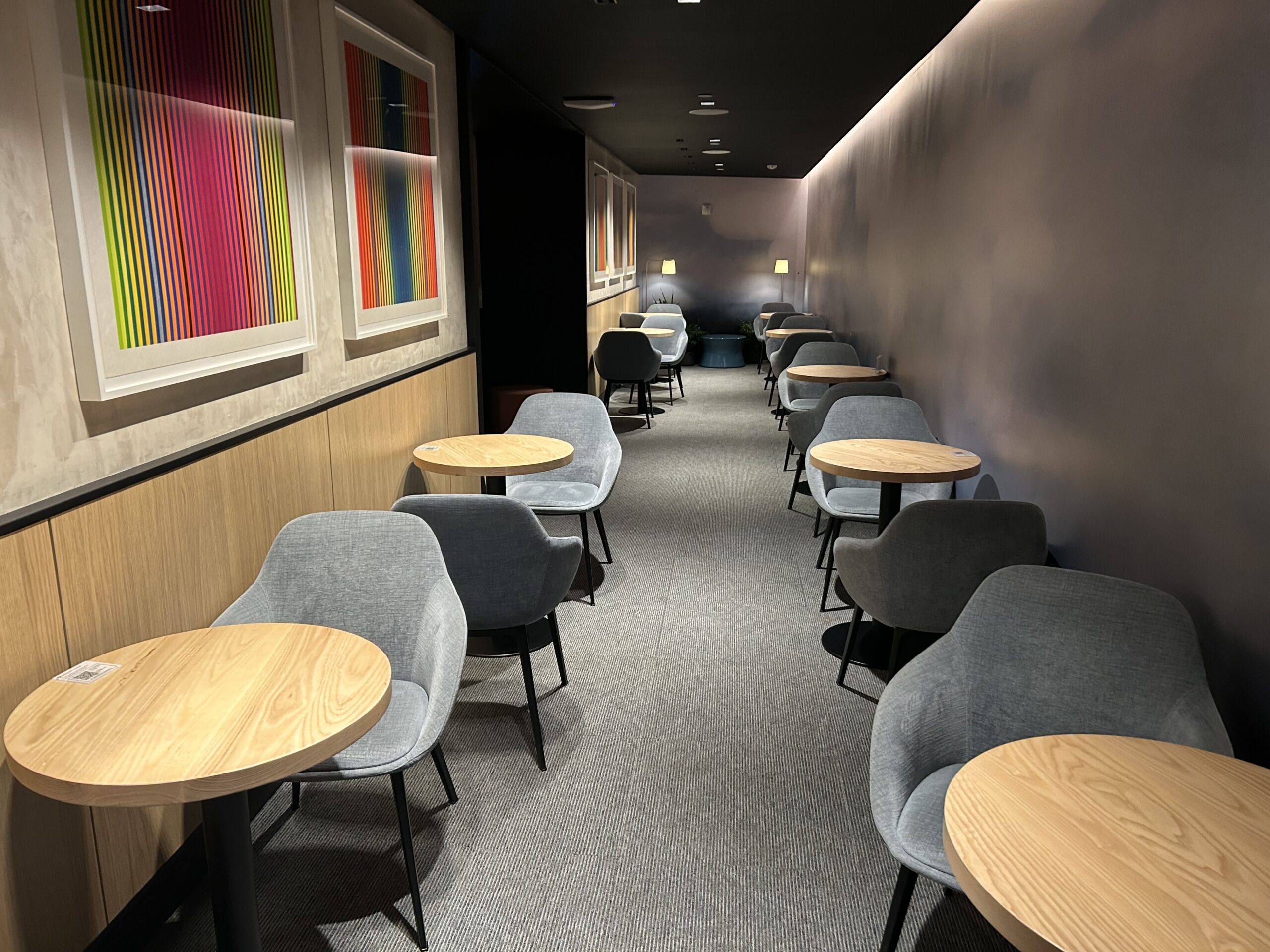 a hallway full of tables inside an airport lounge. 