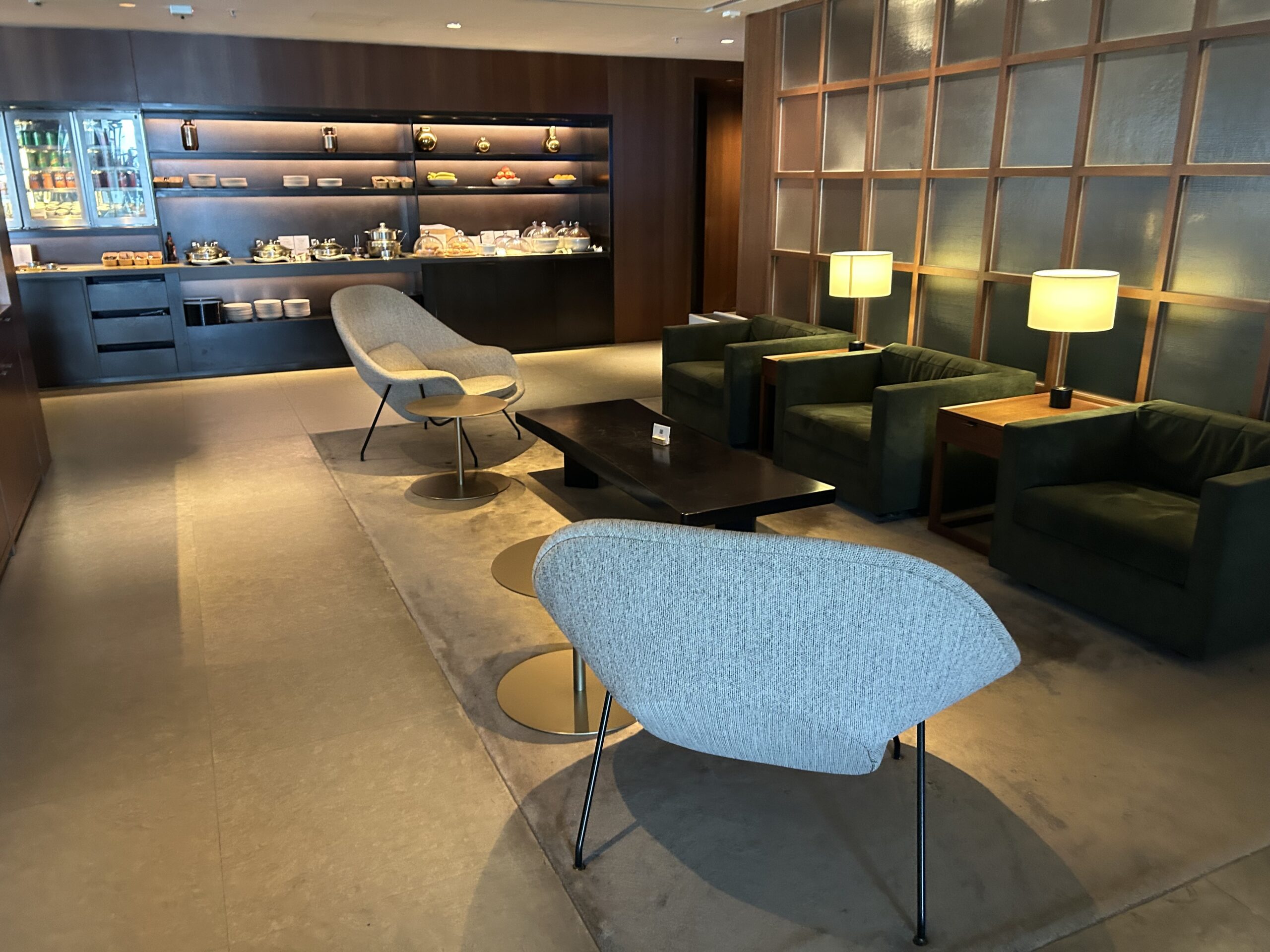 Armchairs inside an airport lounge. There is a display of food and drinks along the back wall. 