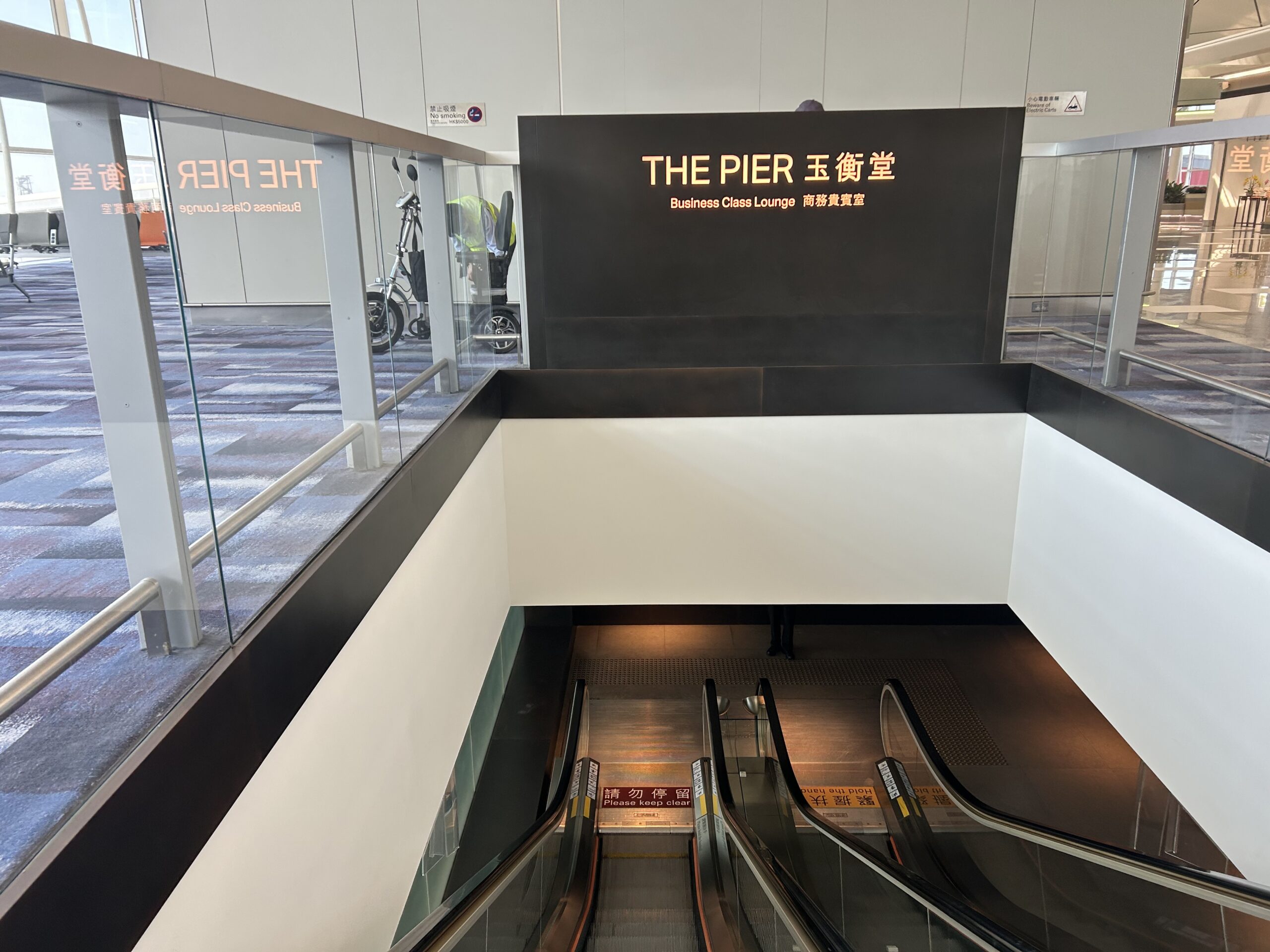 A sign indicating The Pier Business Class Lounge and an escalator to leading to the lower level. 