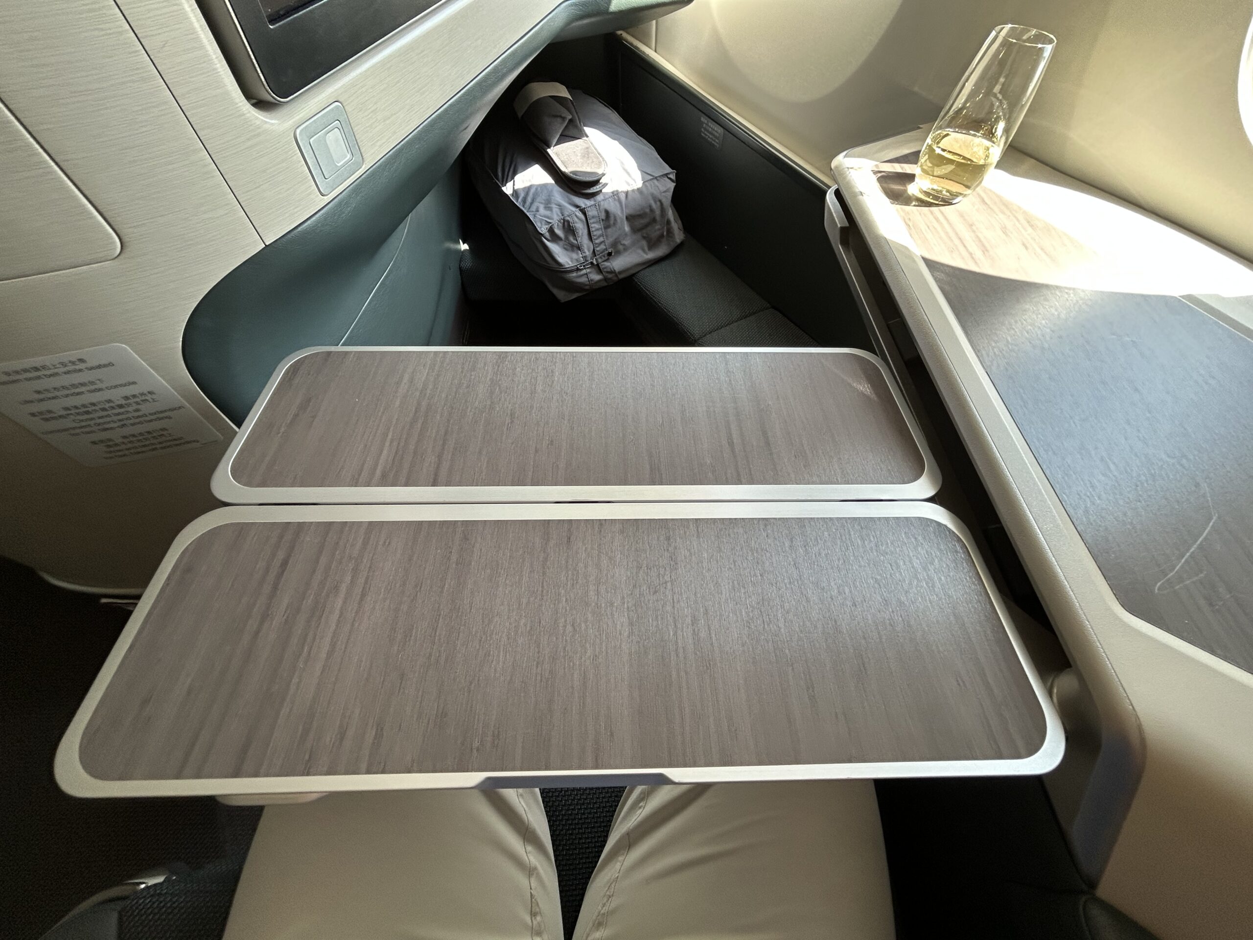 Tray table on an airplane. There's a glass of champagne sitting in the sunlight on the console table to the right. 