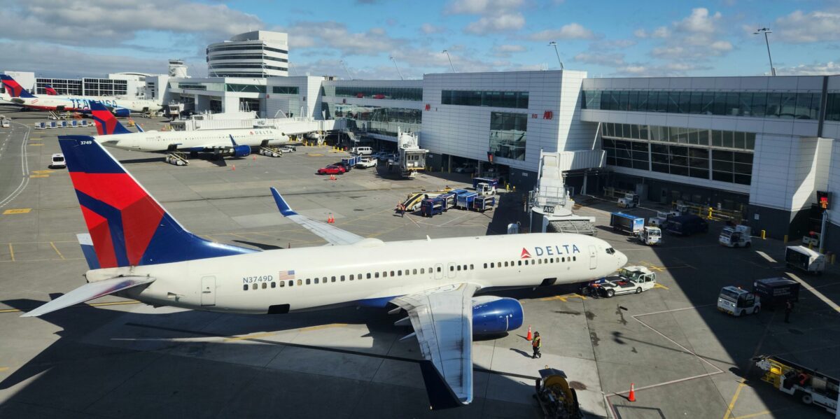 a delta plane at an airport gate with several other planes in the background