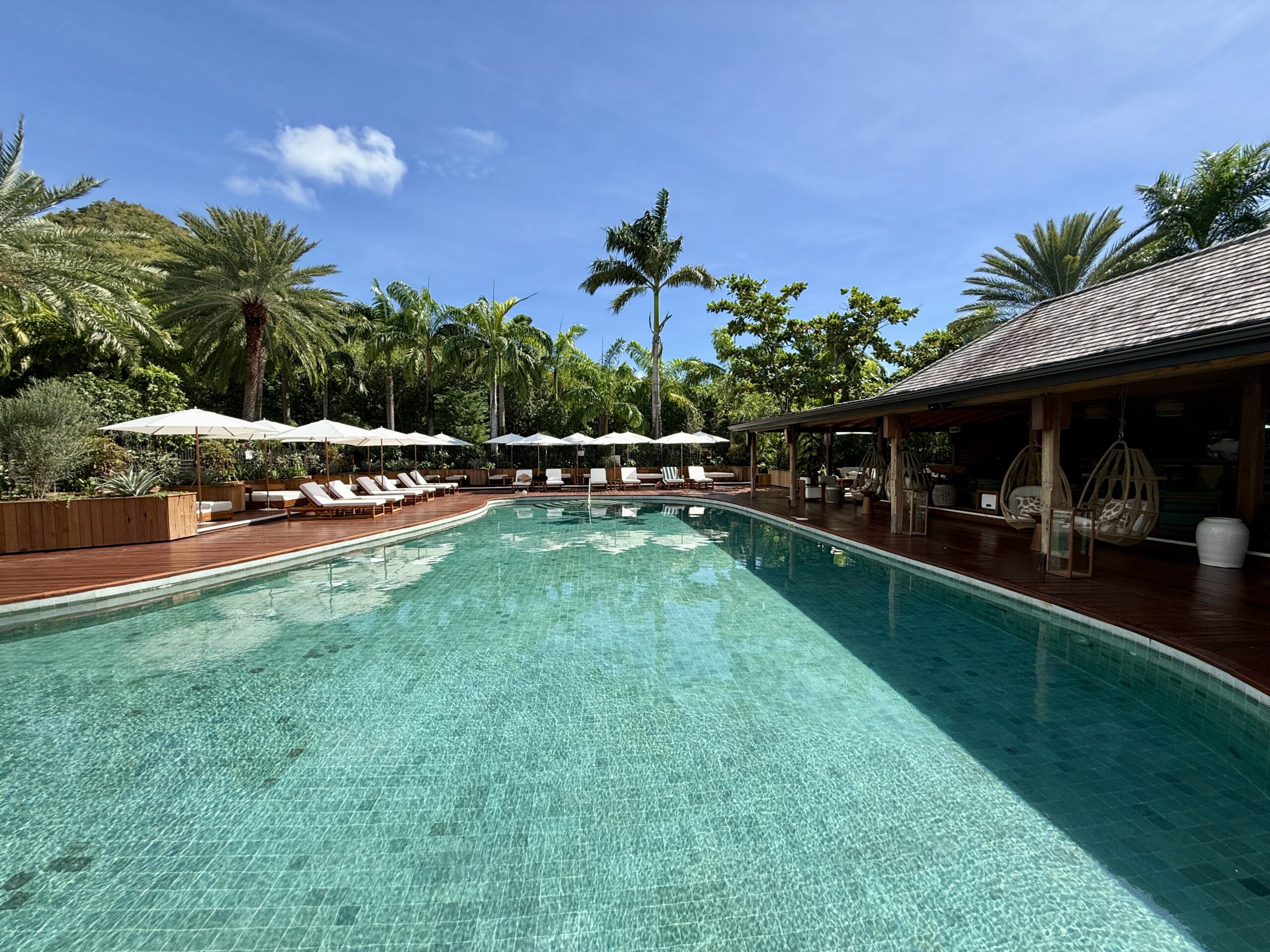 a pool with tile floors surrounded by a deck with chairs and a bar