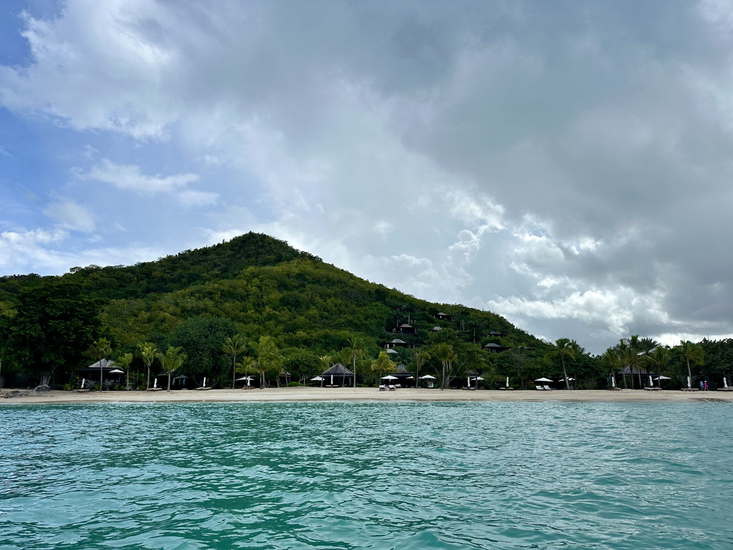 a coastline with a lush green hill and several villas pictured from the water
