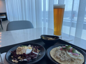 a tray with a salad and tostada with a glass of beer behind it