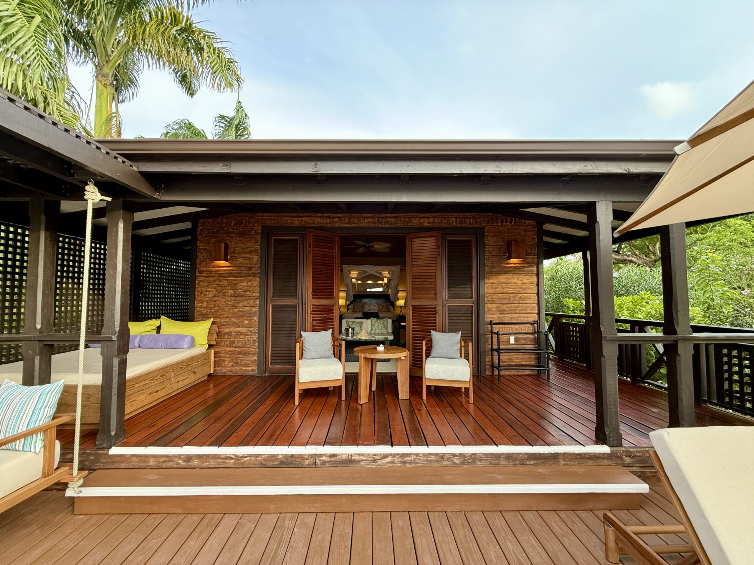 chairs, table and daybed on a large outdoor deck outside of a villa