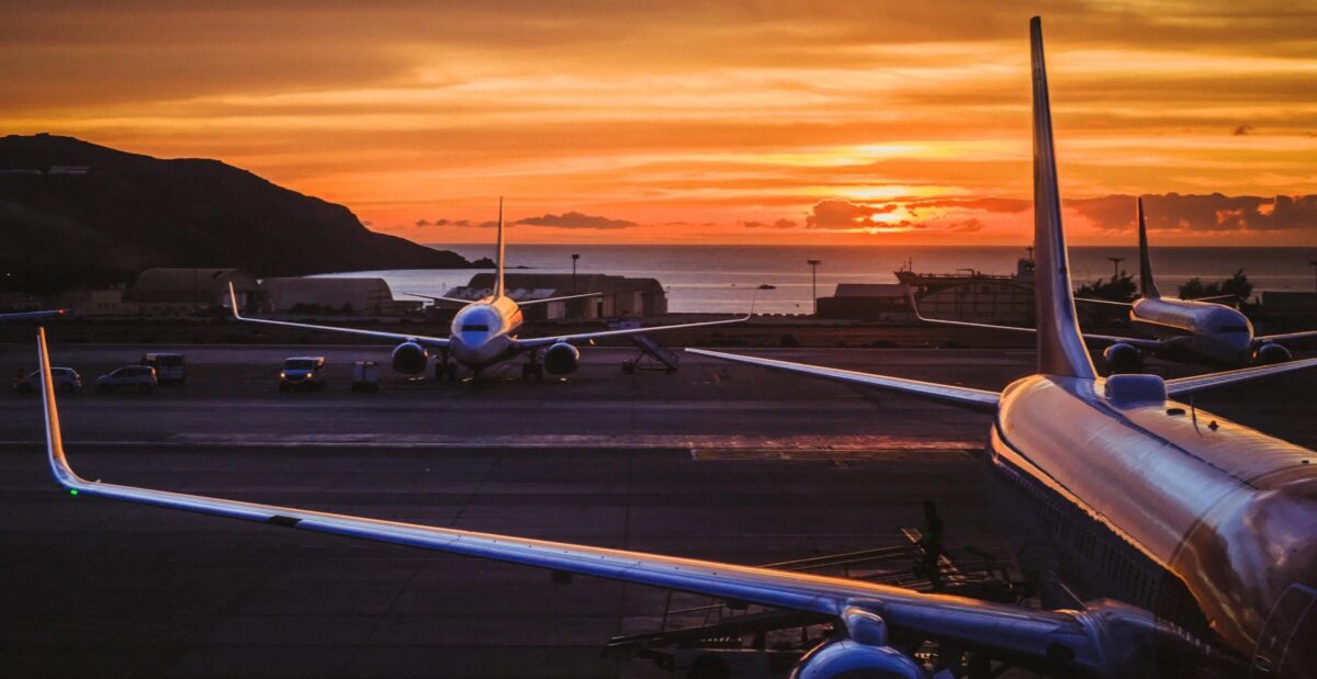 three planes on the tarmac with the sun rising in an orange sky