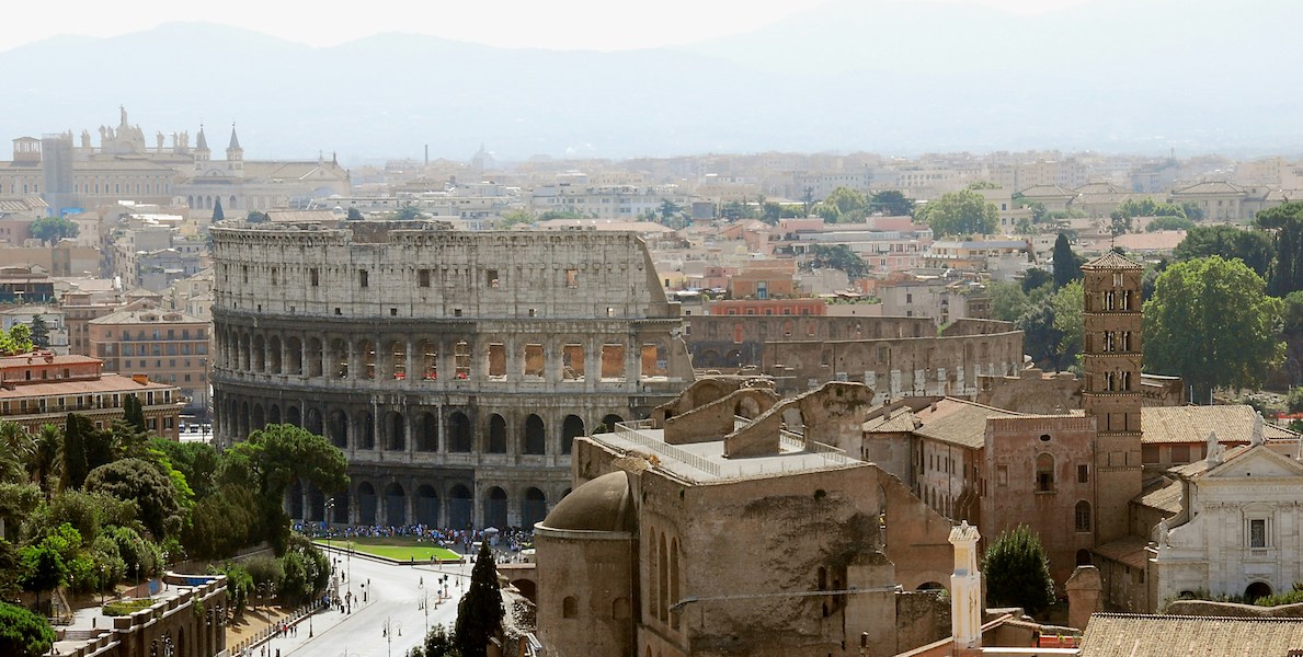 the roman colisseum surrounded by other buildings in rome with mountains in the background.