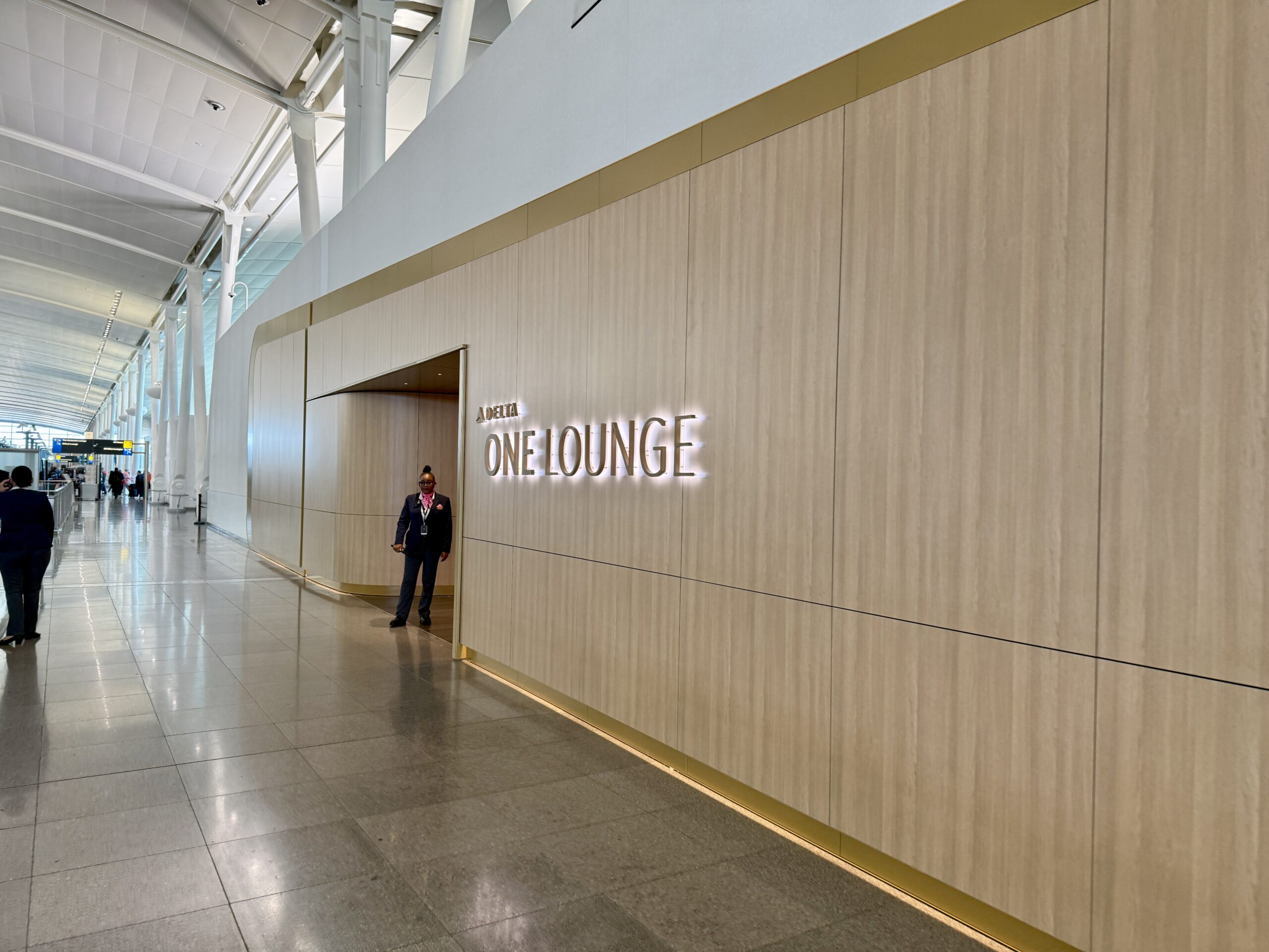 delta one lounge entryway in soft woods with gold white accents. An employee is waiting by the entrance. 